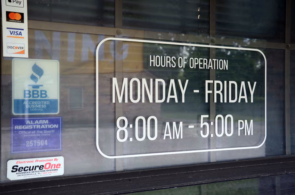 Storefront window displaying hours of operation and payment logos on glass.
