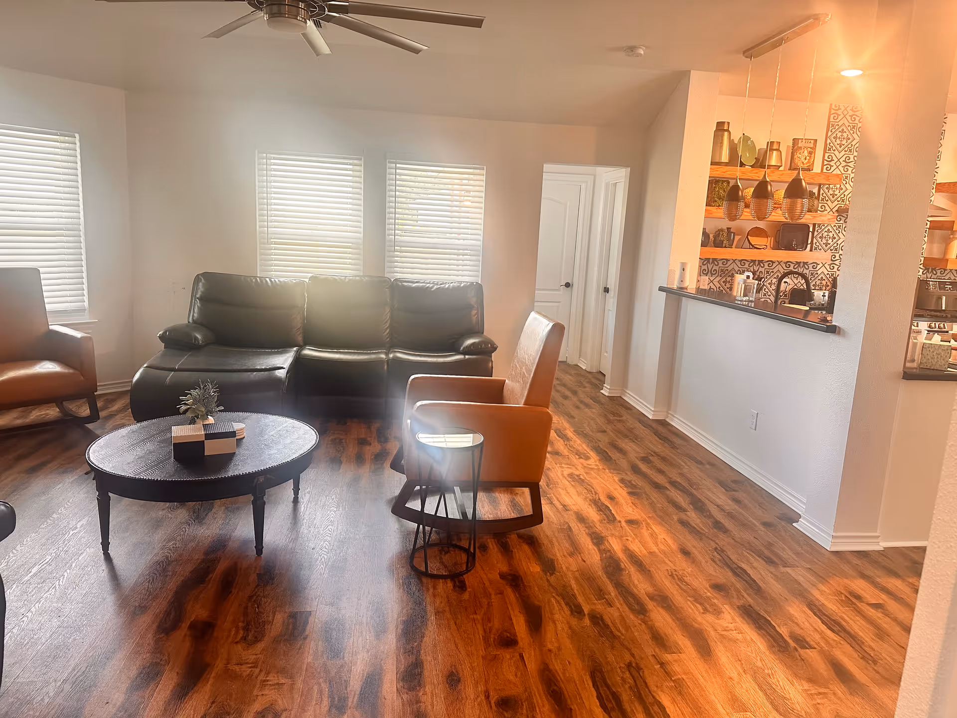 Living room with leather sofa, chairs, coffee table, and open kitchen bar.