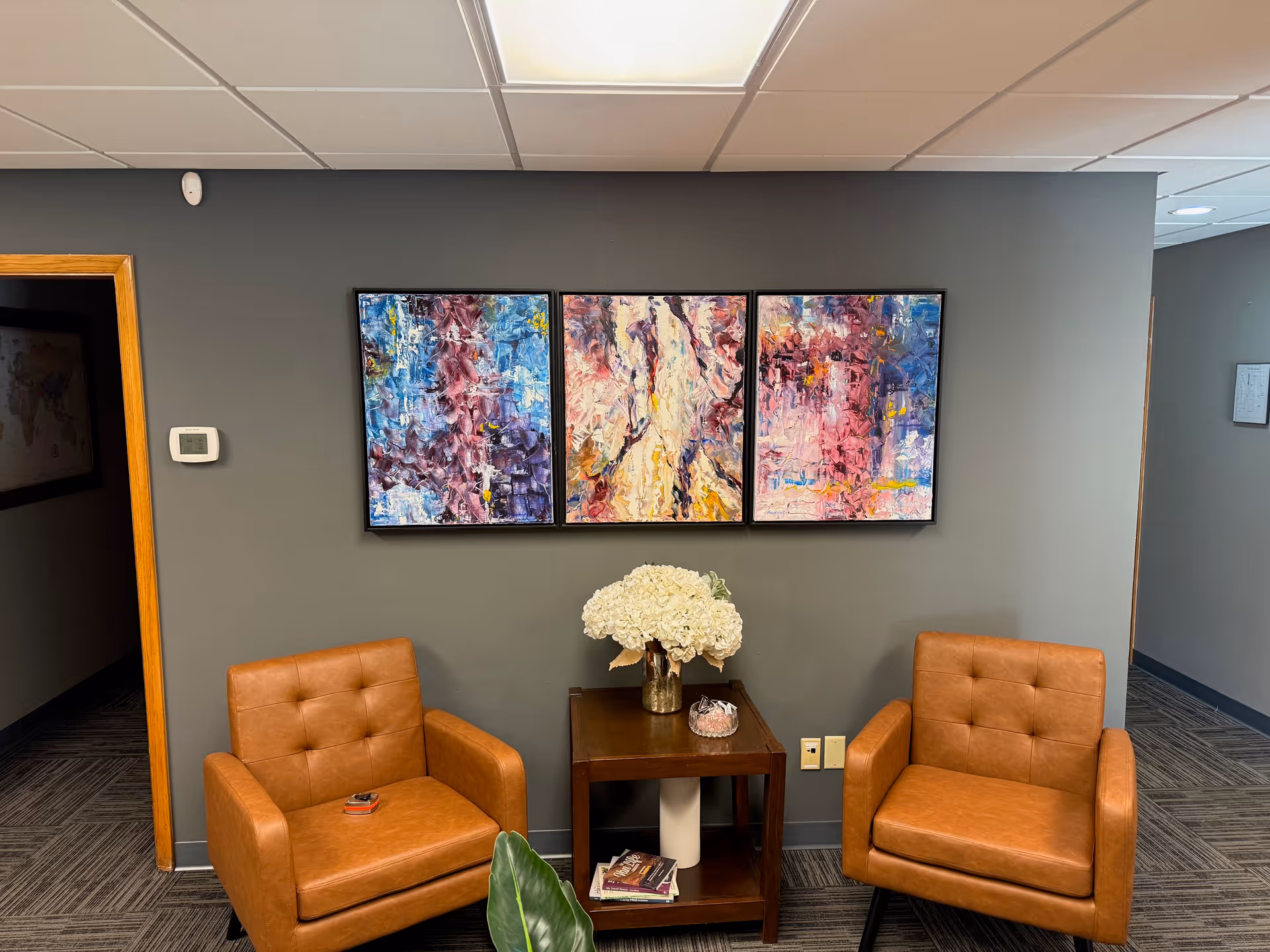 Two tan leather chairs sit beside a small table with white flowers against gray wall.