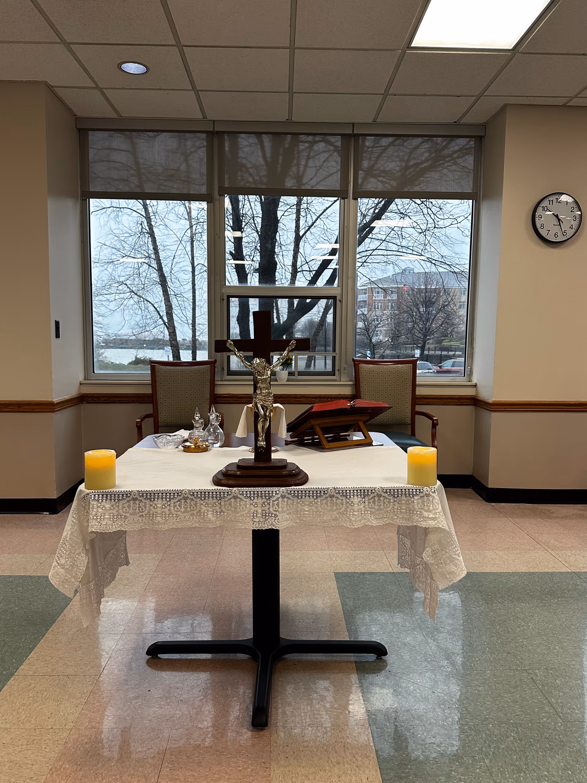 Altar table with crucifix, candles, and lace cloth in a senior living chapel.