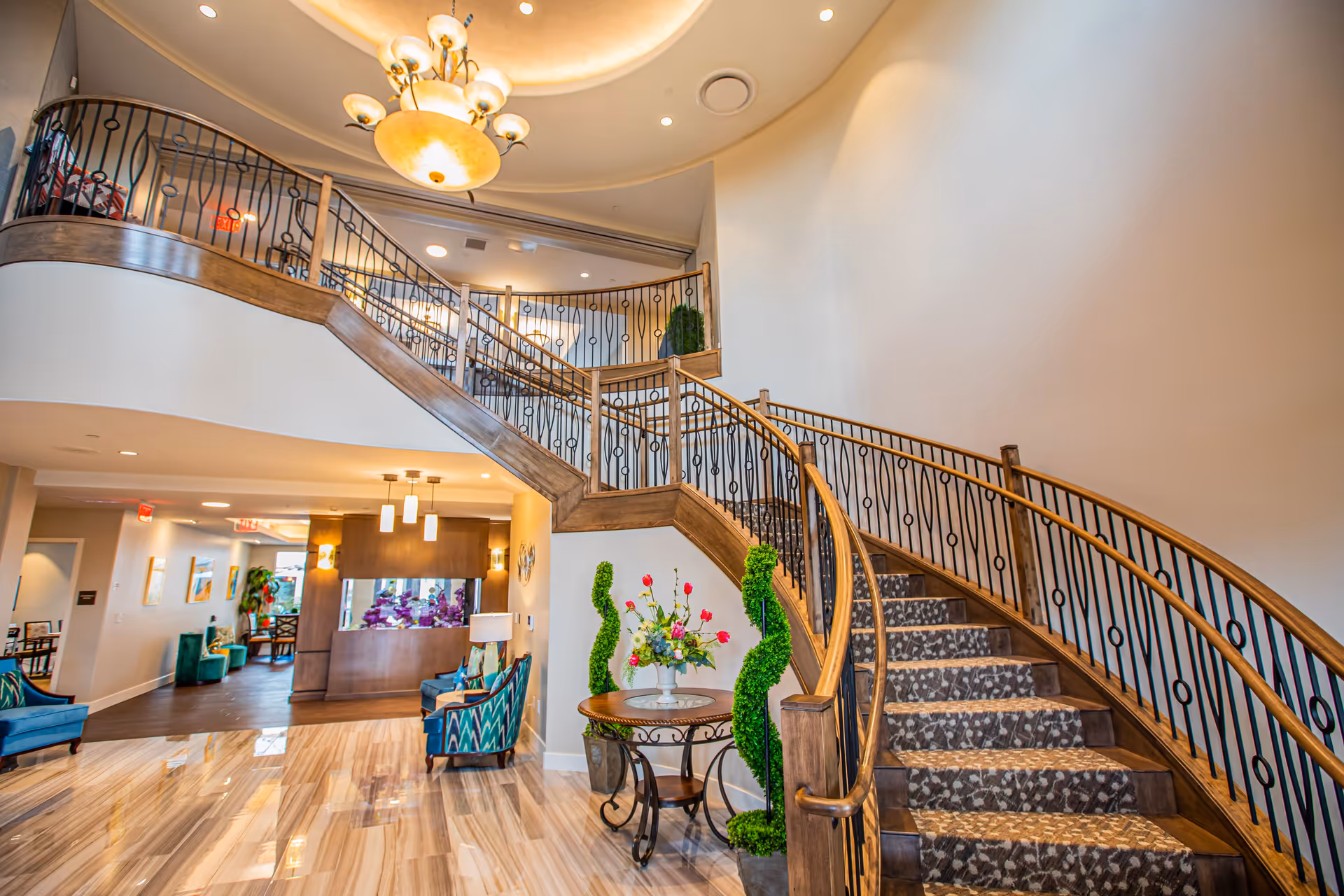 Elegant lobby with a curved staircase, polished floors, seating areas, and a reception desk.