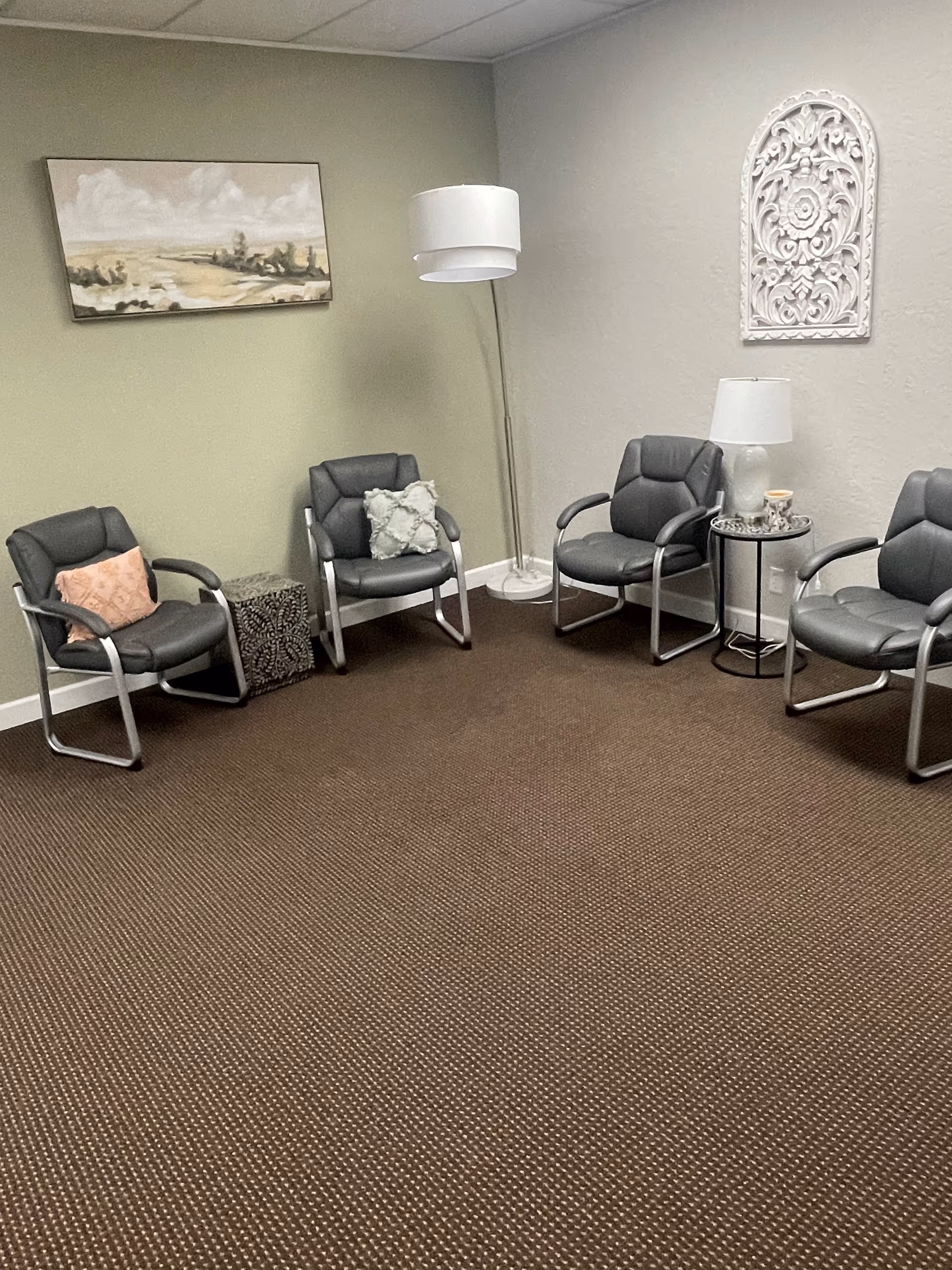 A quiet indoor waiting area with gray chairs, tables, and wall art.