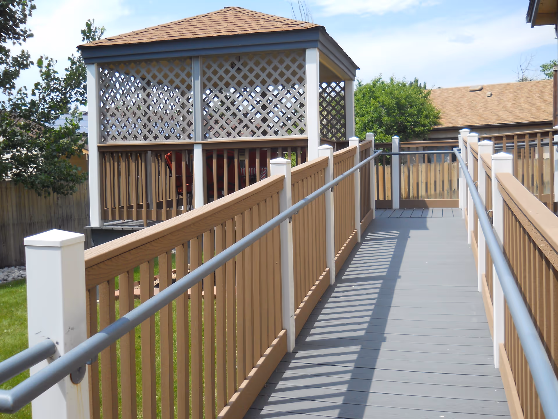 Outdoor elevated walkway with beige railings leads to a lattice gazebo structure.