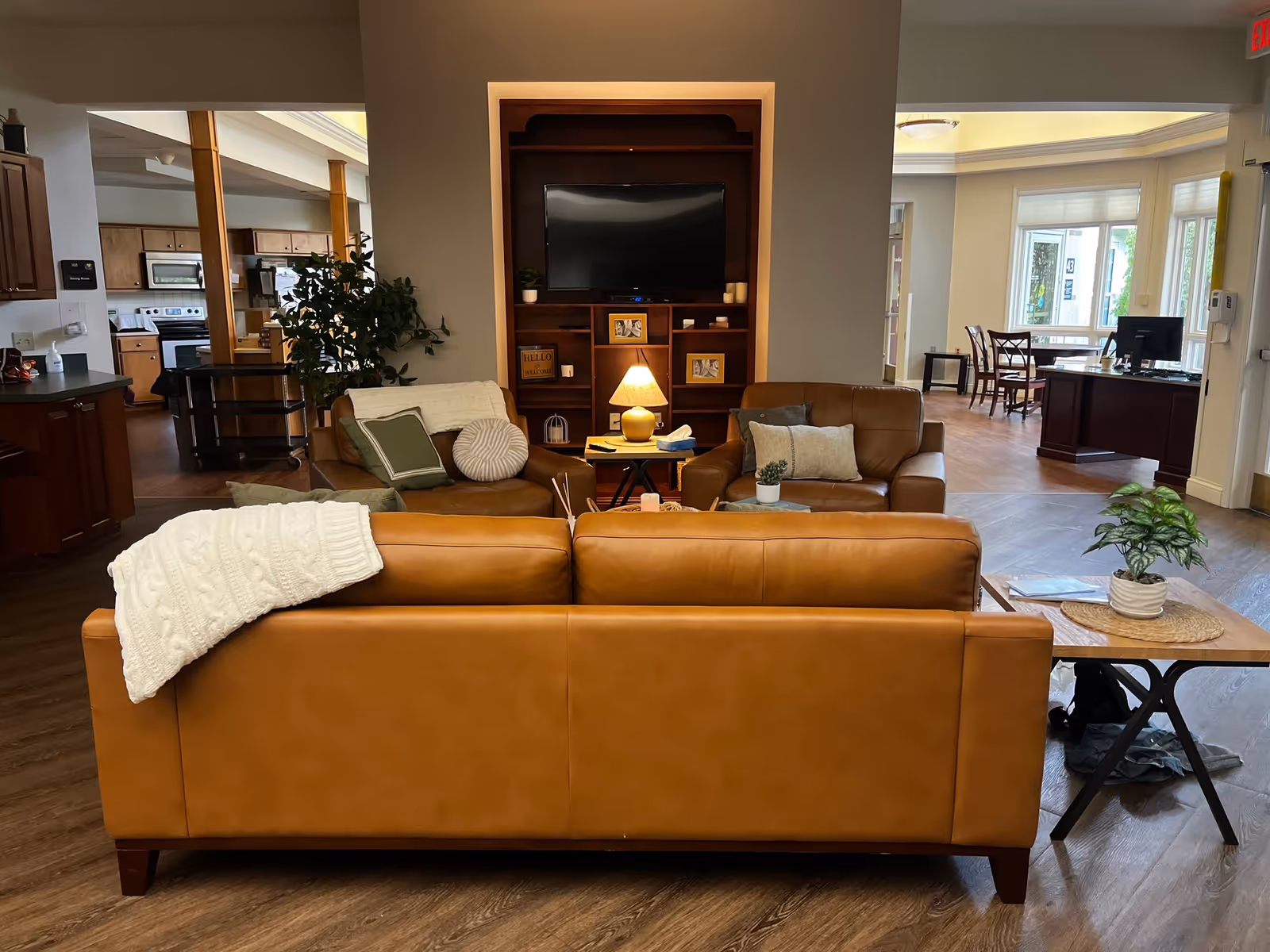 A spacious living room lounge with leather sofas, a TV, and a kitchenette in the background.