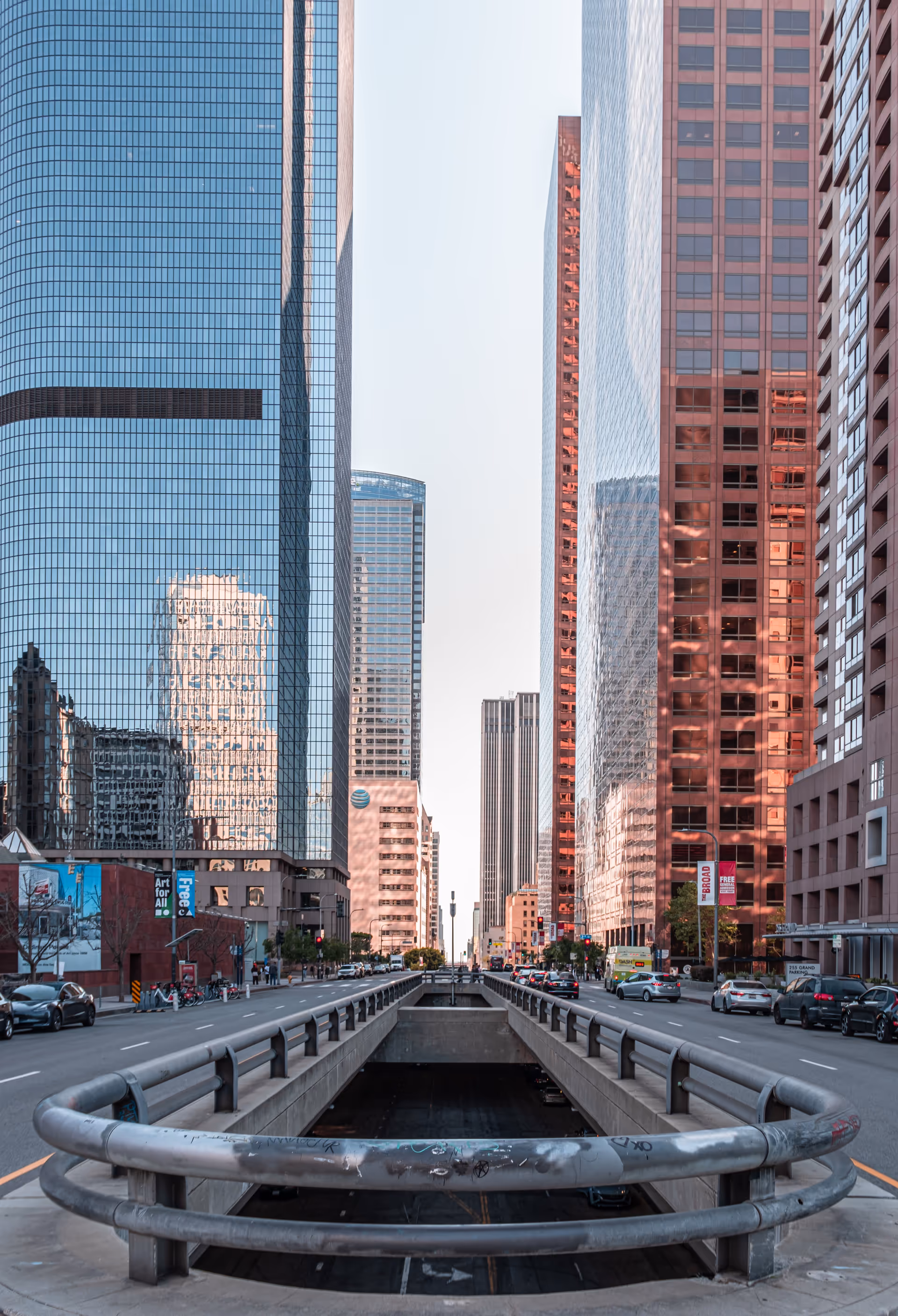 Urban street scene with tall glass skyscrapers on both sides and a sunken roadway.