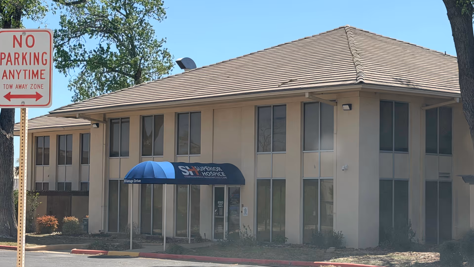 Two-story beige building with blue awning at entrance labeled Superior Hospice; no parking sign visible.