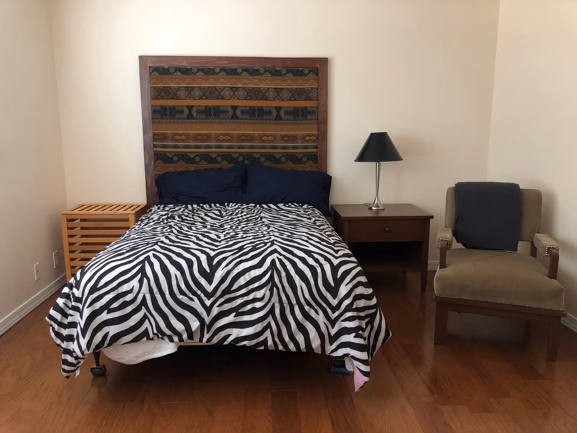 Bedroom with a zebra-patterned bedspread, wooden headboard, nightstand, lamp, and chair.