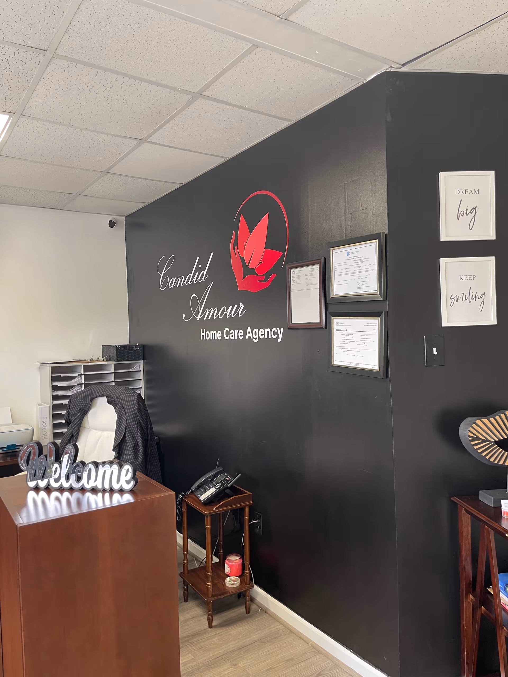 Reception area of Candid Amour Home Care Agency with black wall, logo, and welcome desk.