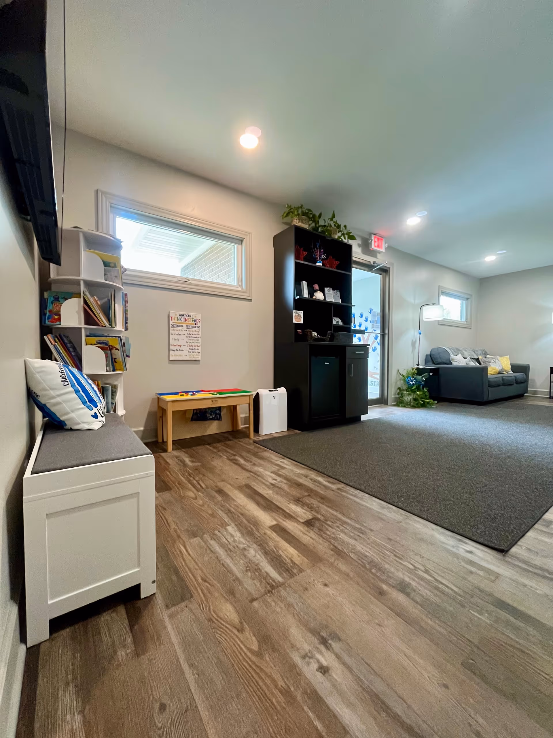 Bright common area with bench seating, bookshelf, black cabinet, and a gray sofa.