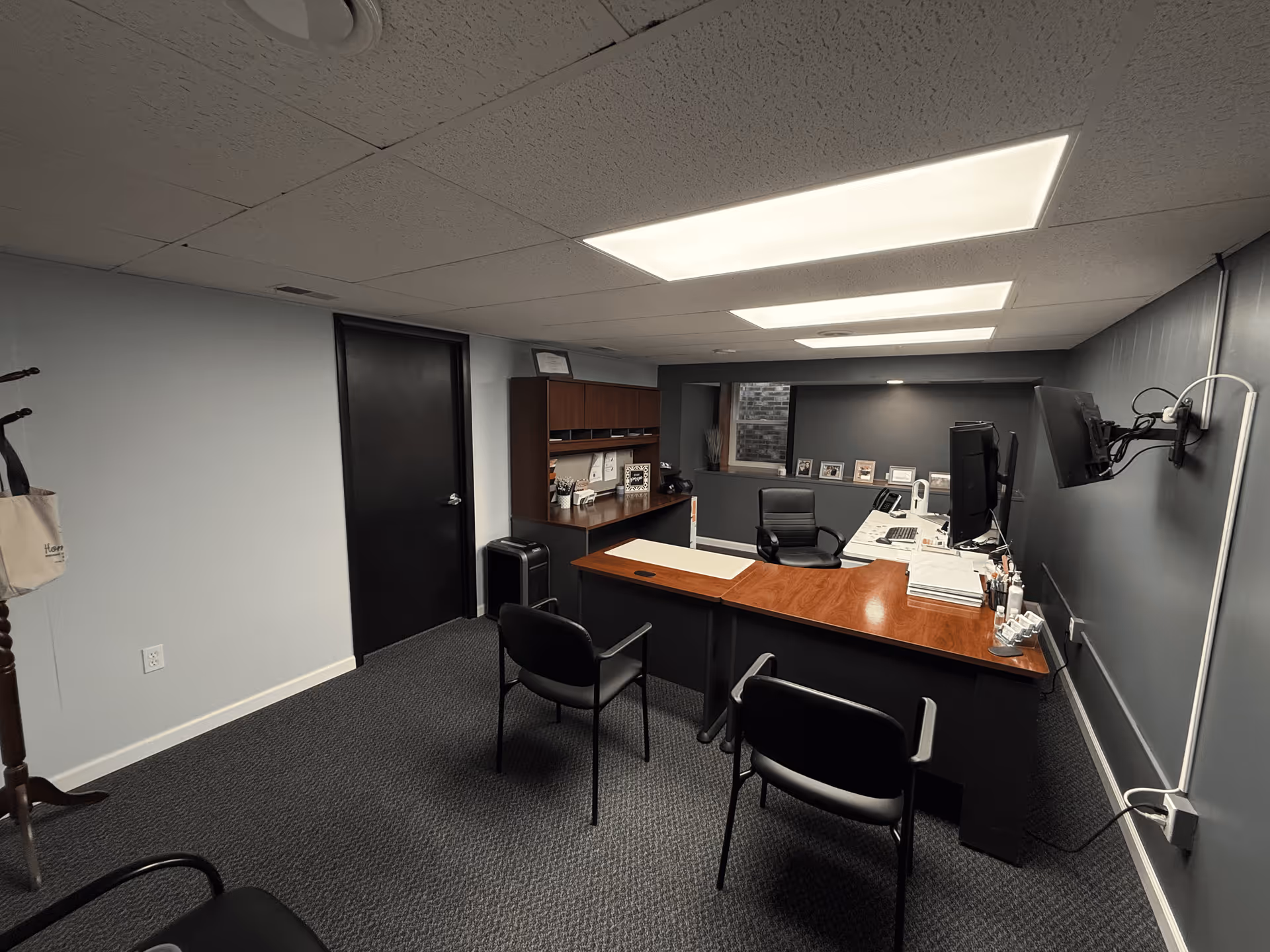A small office with a wooden desk, computer, chairs, and filing shelves.