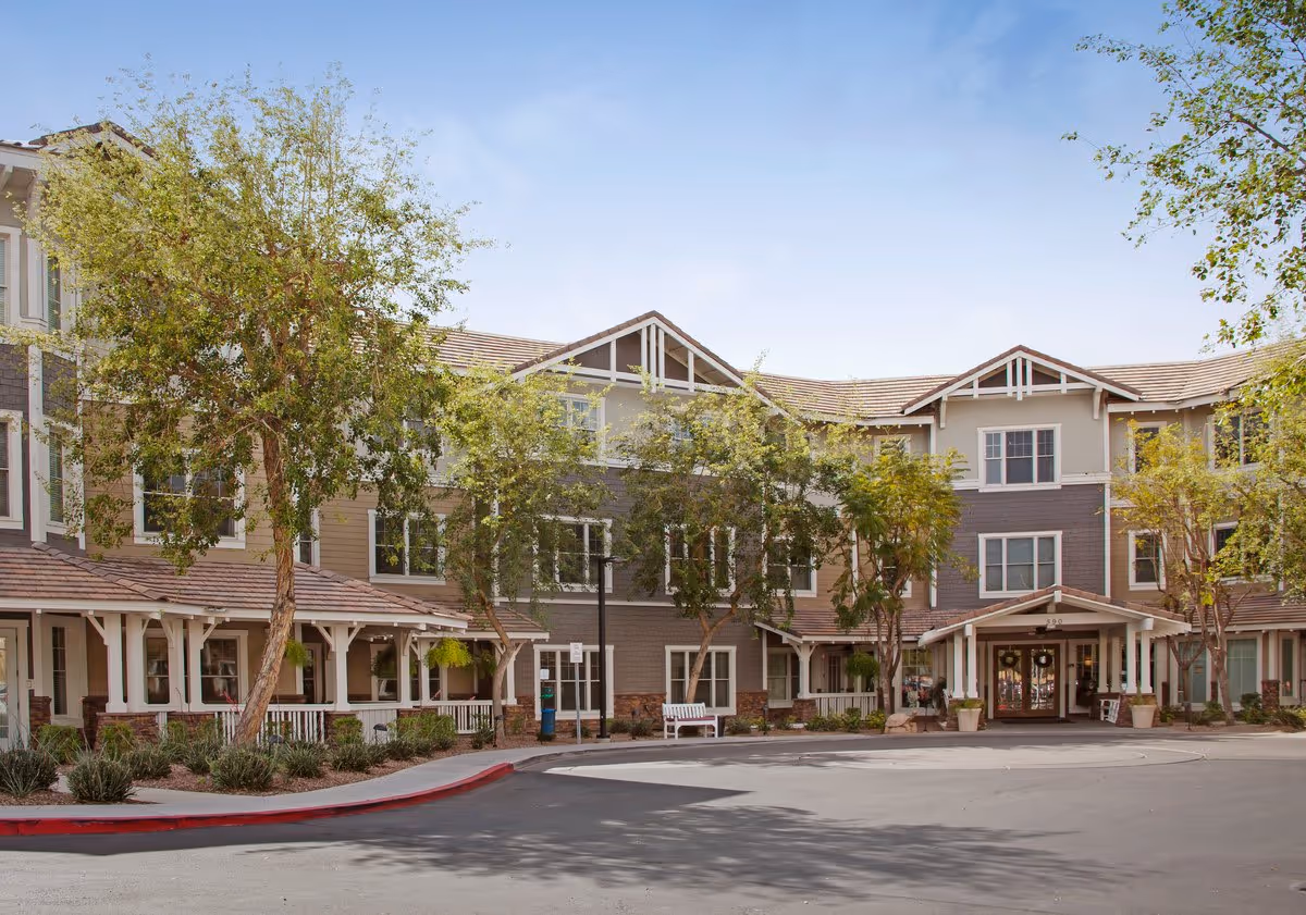Front exterior of a three-story senior living facility with a covered entrance, trees, and a circular driveway.