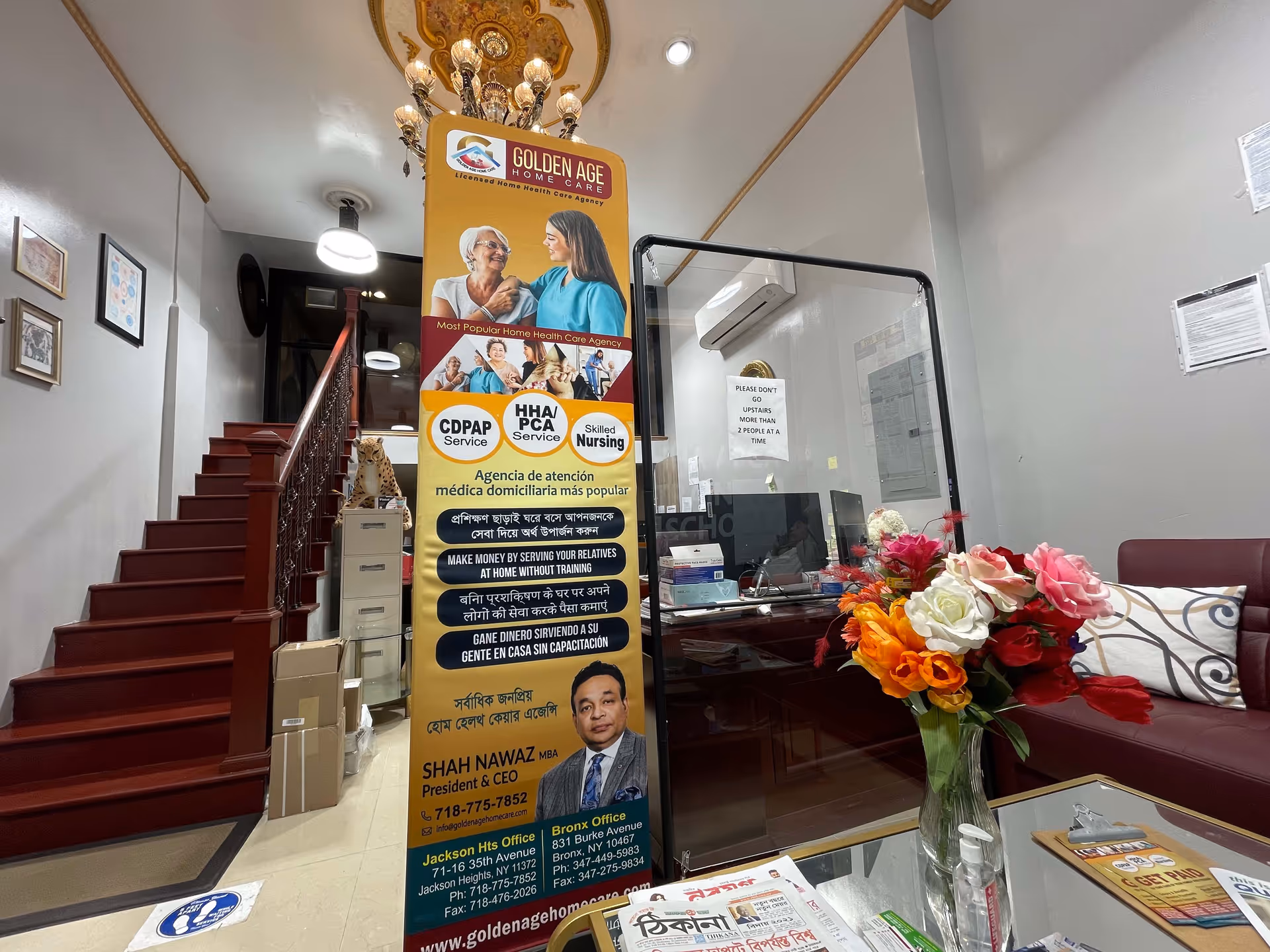Lobby area of Golden Age Home Care with banner, glass desk, stairs, and flowers.