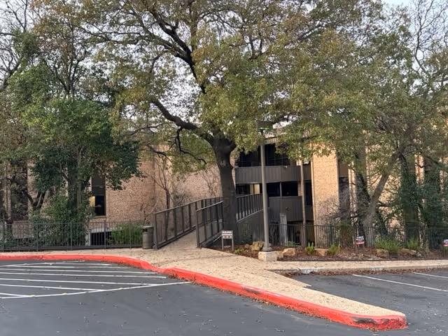 Exterior view of a brick senior living facility entrance with a ramp and trees.