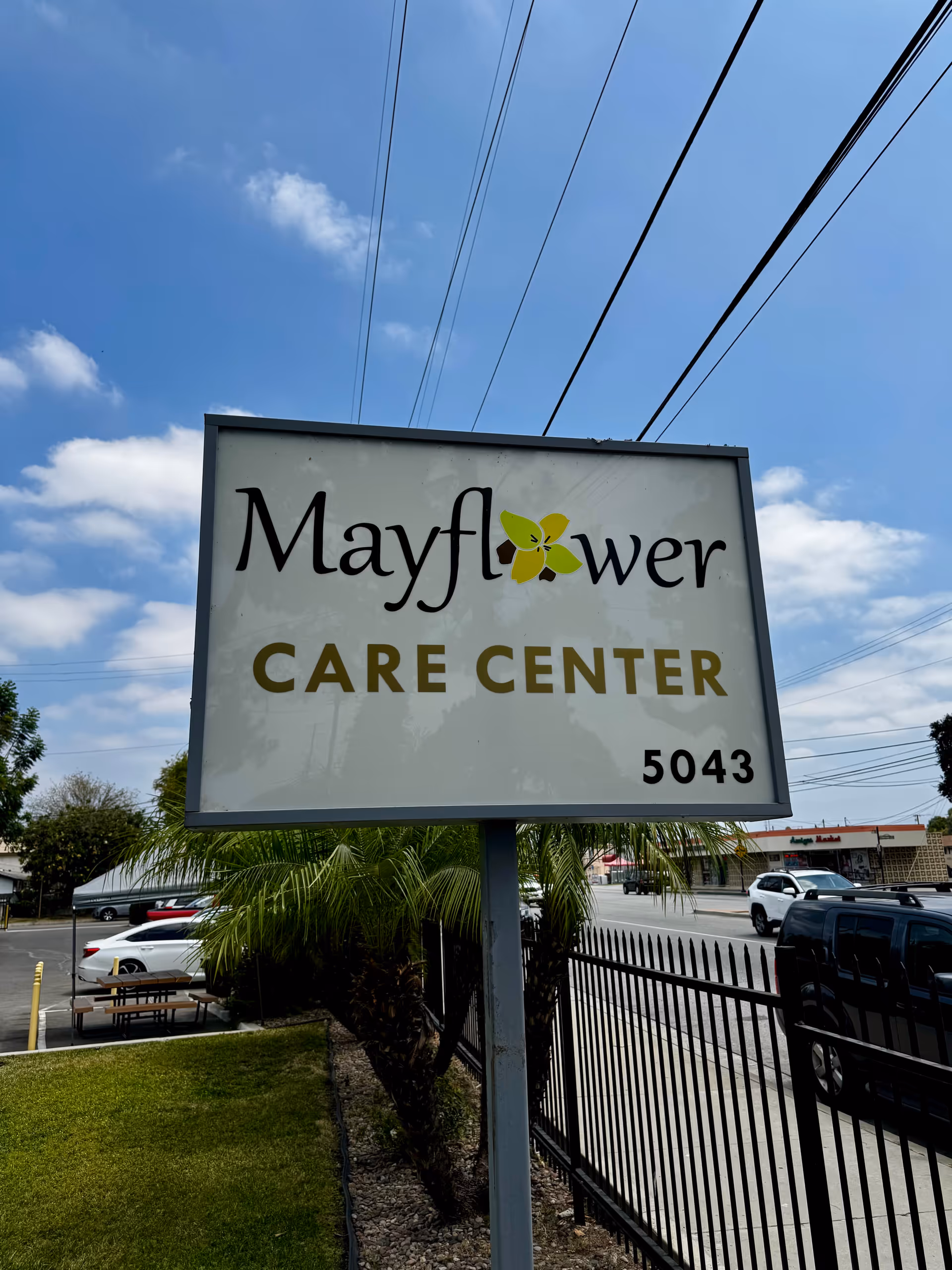 Mayflower Care Center sign on a pole with power lines and parked cars nearby