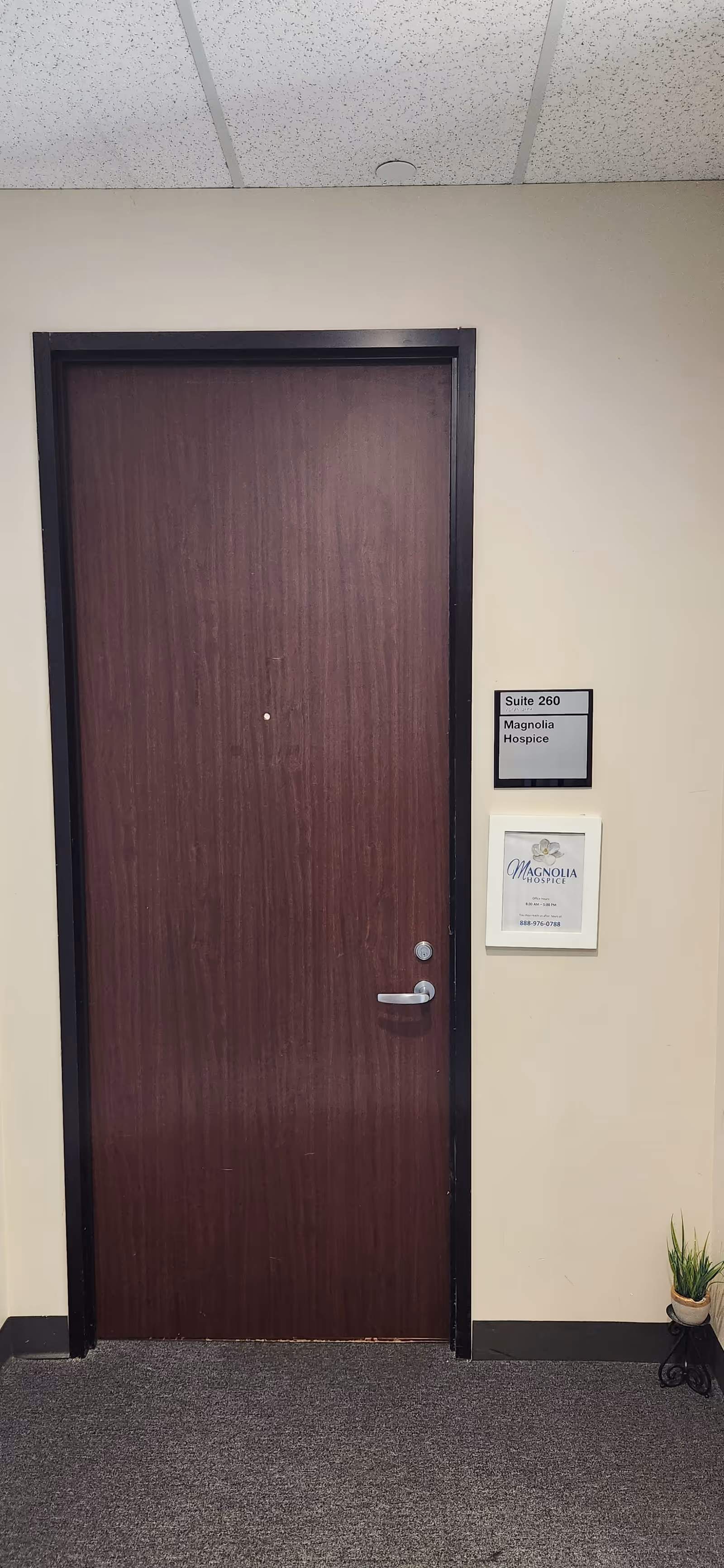 Closed wooden door in a beige hallway beside Magnolia Hospice suite sign.