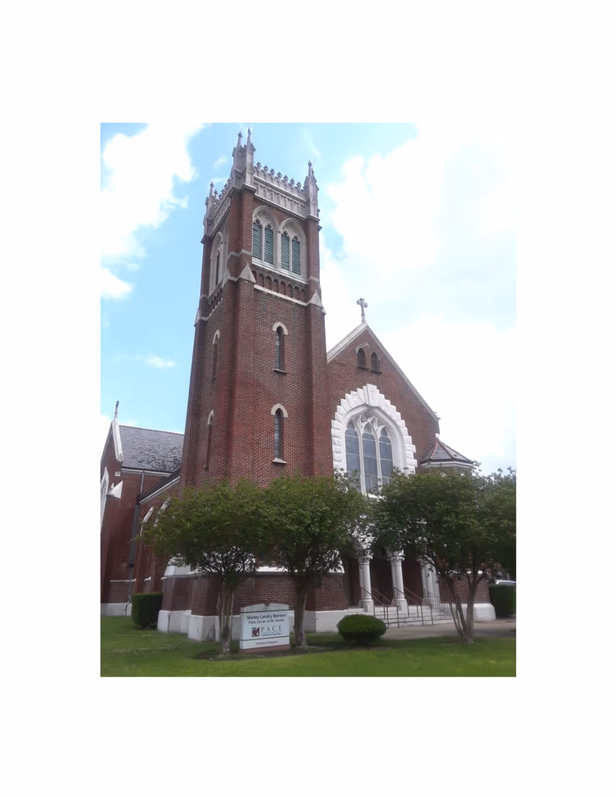 Brick church-style senior living building with towers, trees, and a sign at the entrance.