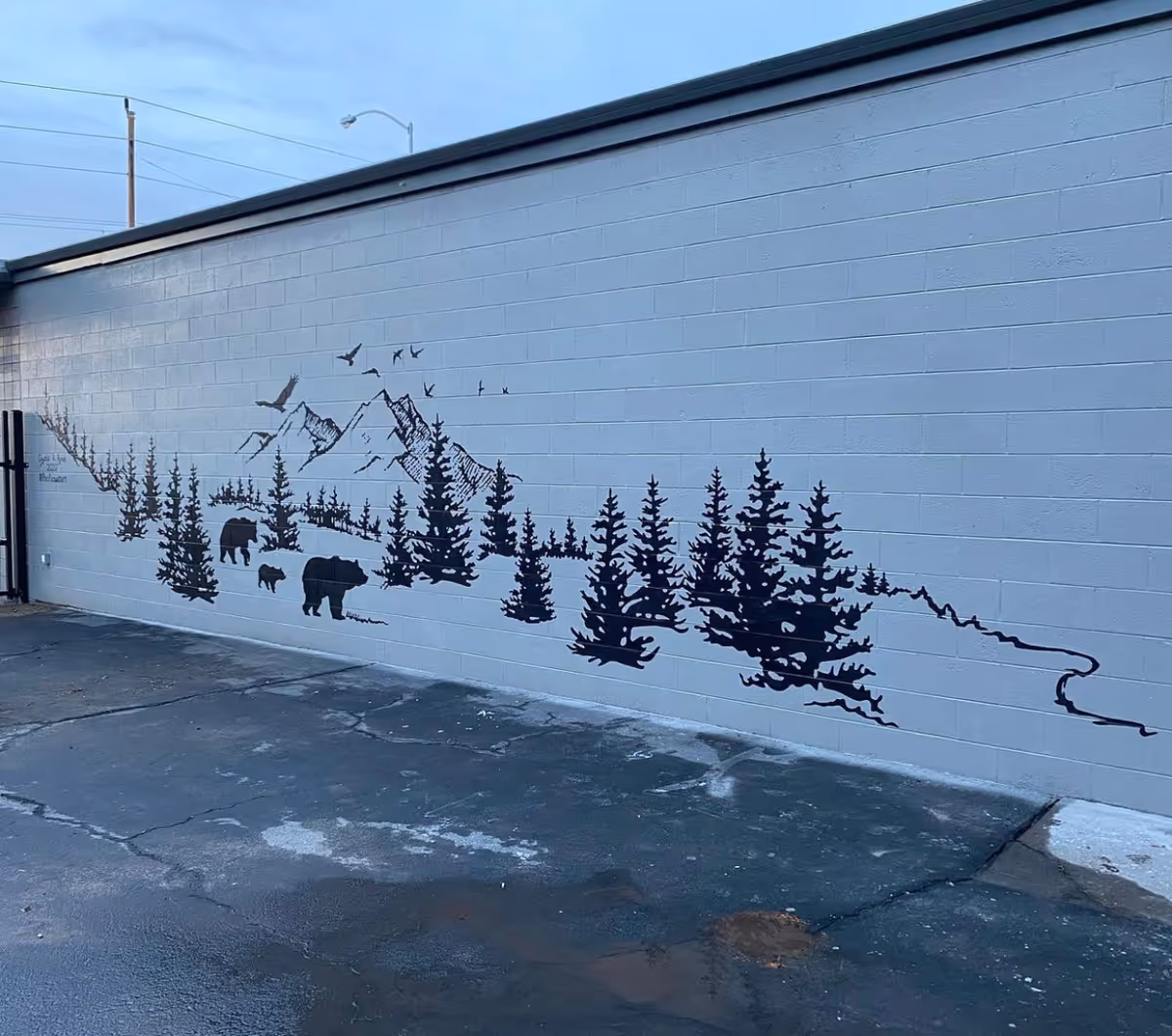 Exterior building wall with a mountain and forest mural featuring trees and bears.