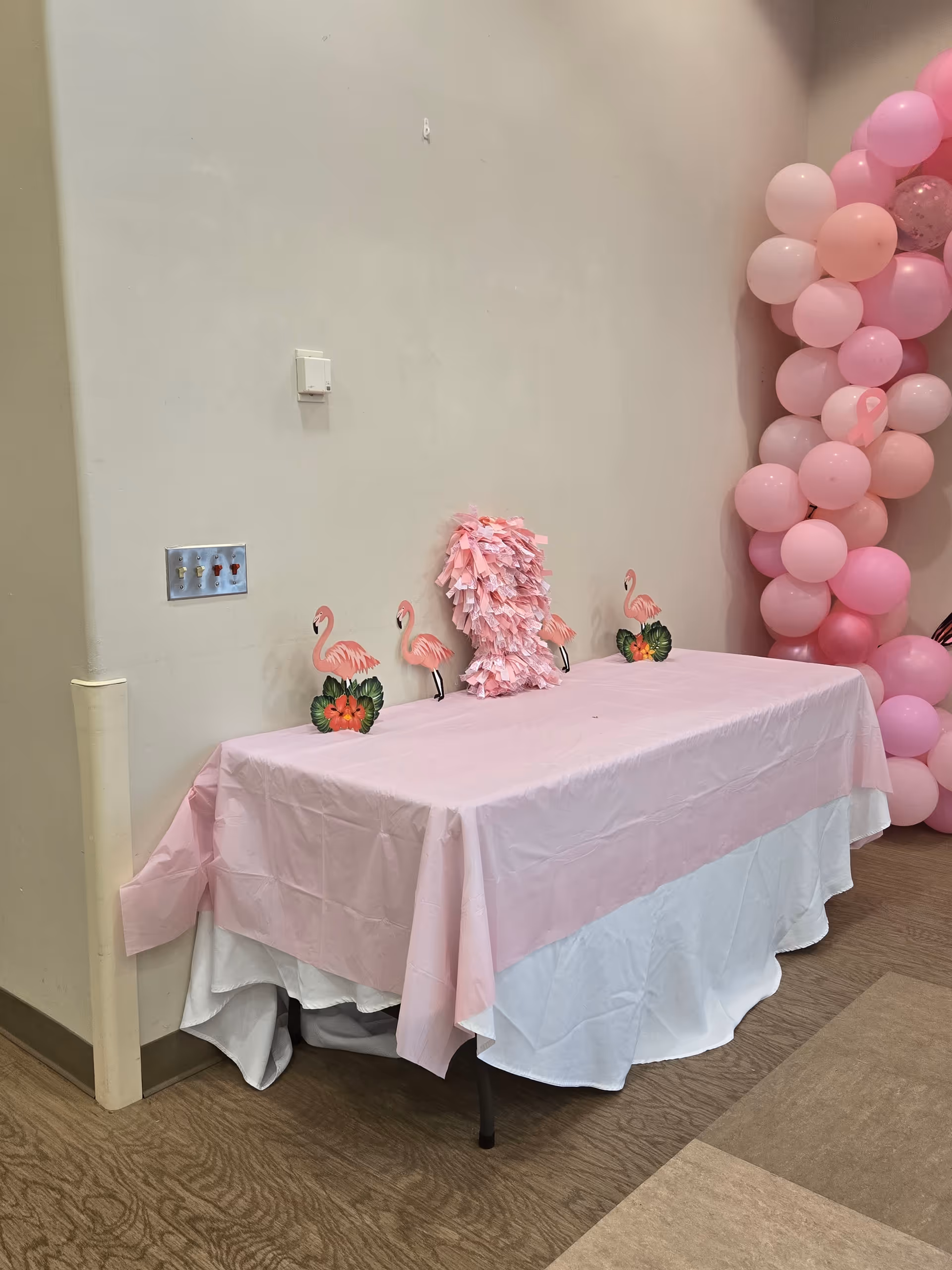 A pink-themed party table with flamingo decorations and a pink balloon arch indoors.