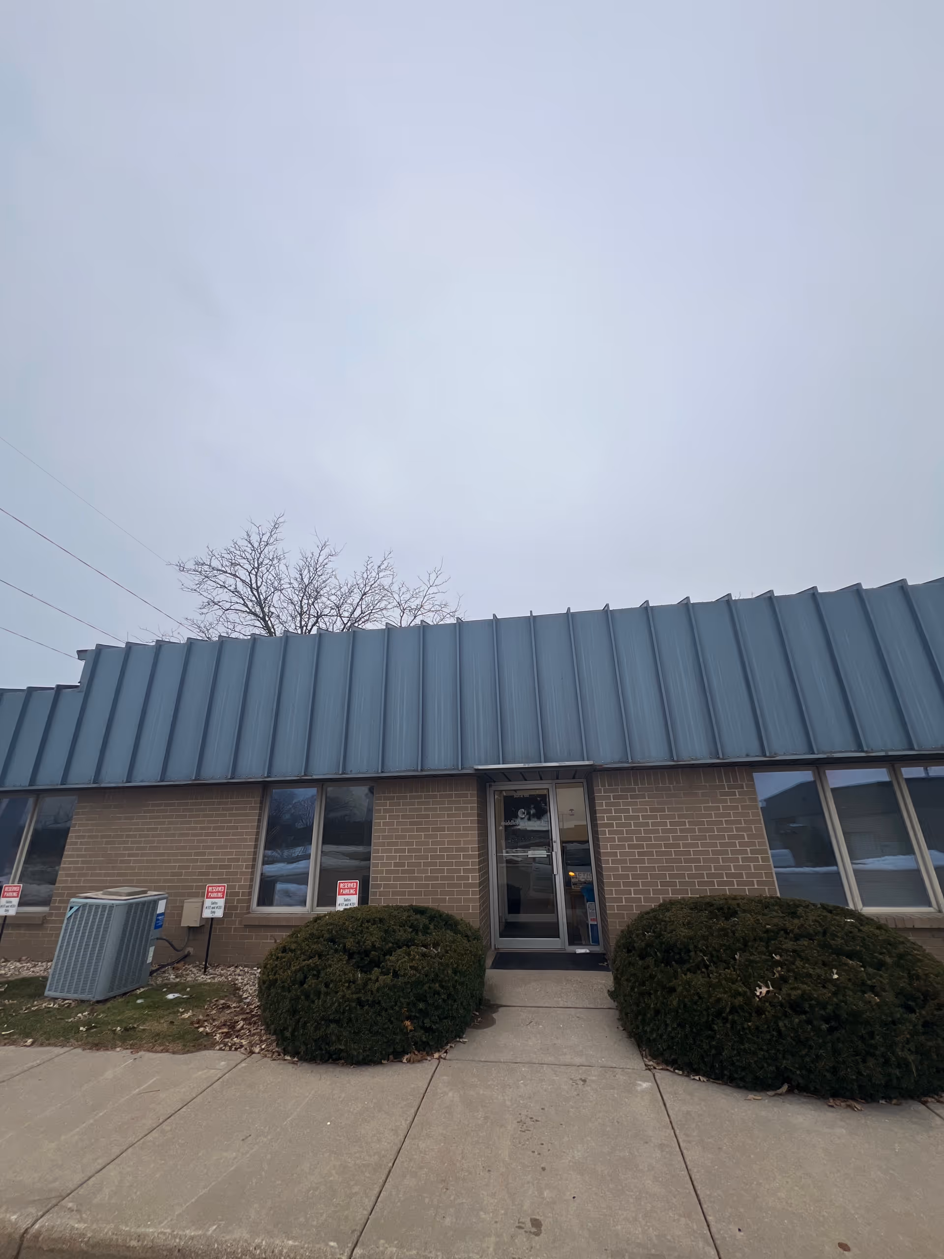 Front view of Shifa Home Healthcare Inc building with glass doors and shrubbery.