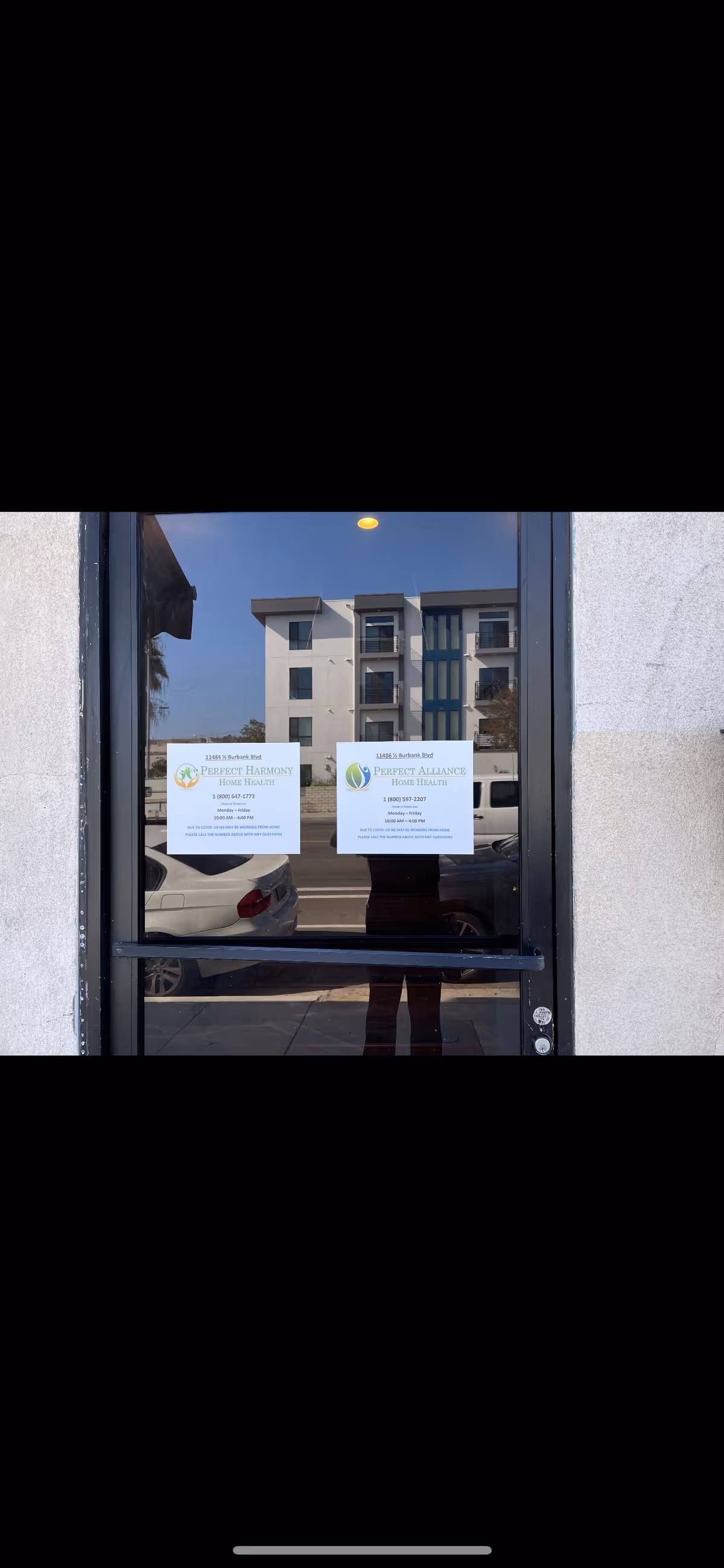 Glass door displays two notices; reflection shows a parked car and nearby building.