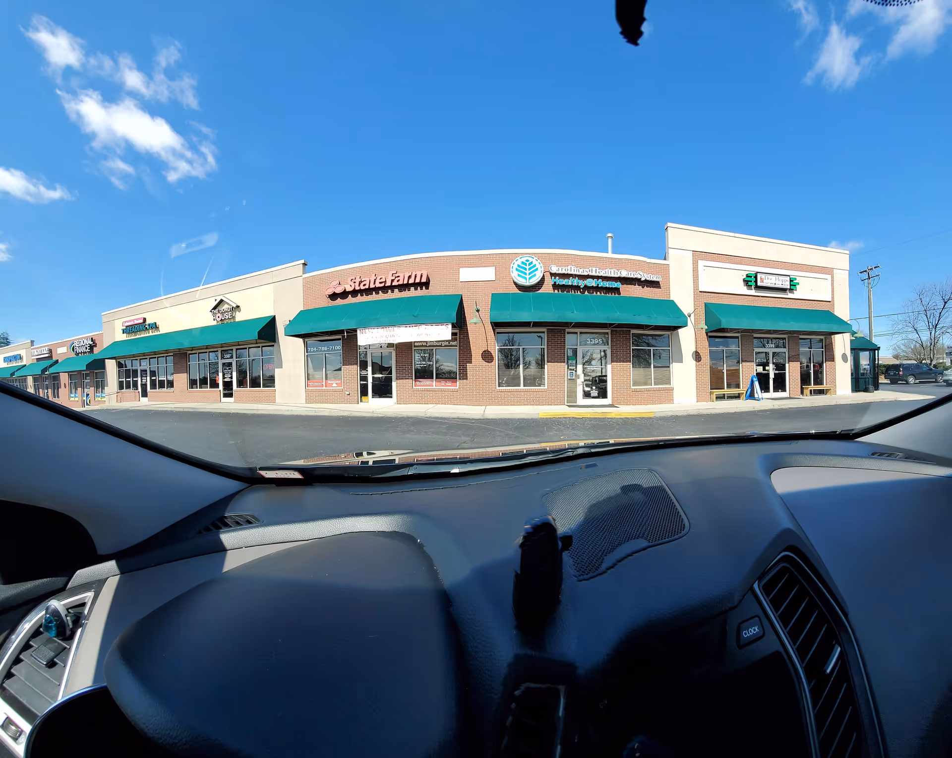 Front view of a strip mall with storefronts and green awnings, seen from inside a car.