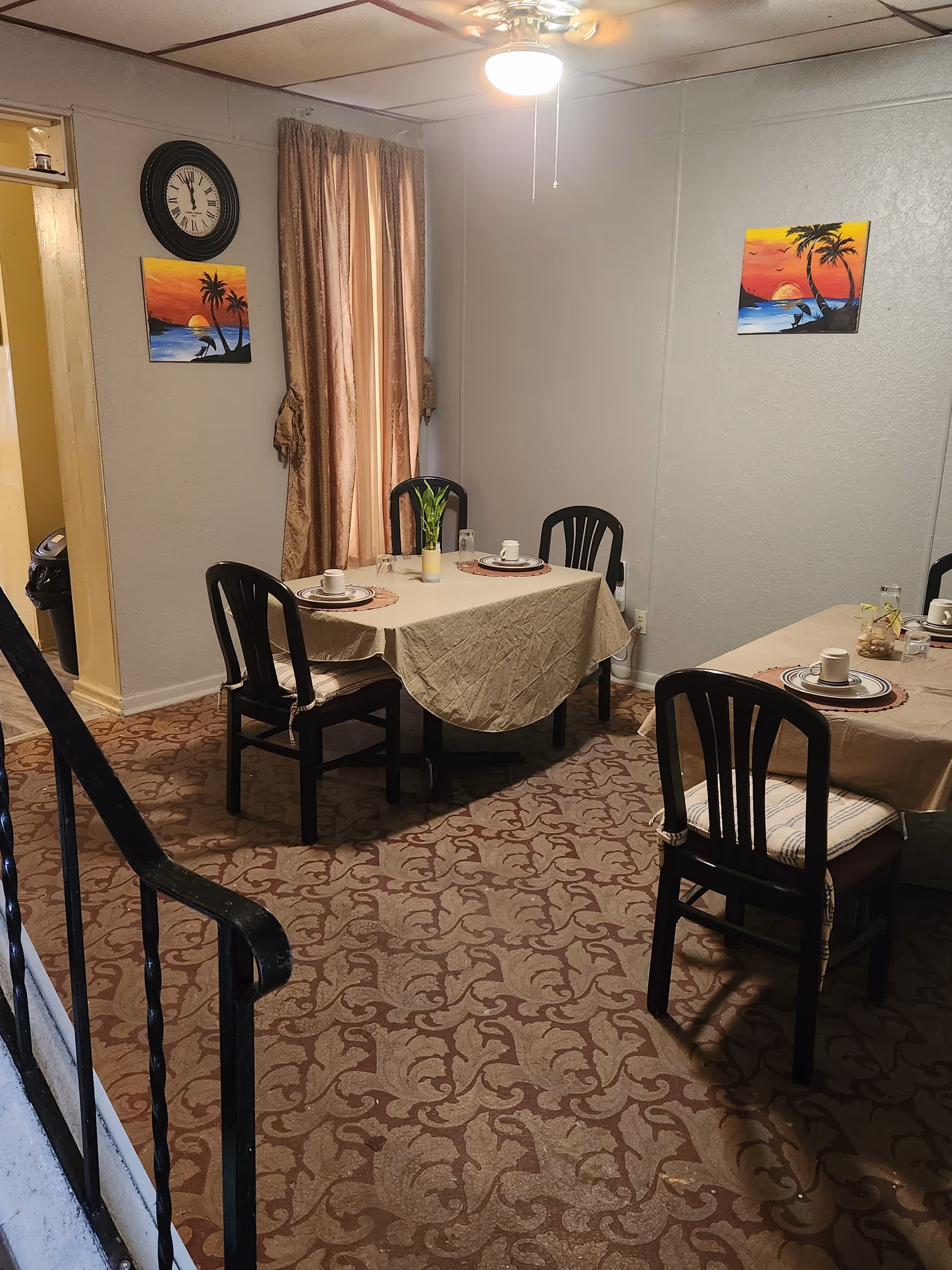 A small dining room with two tables set for meals, chairs, and tropical wall art.