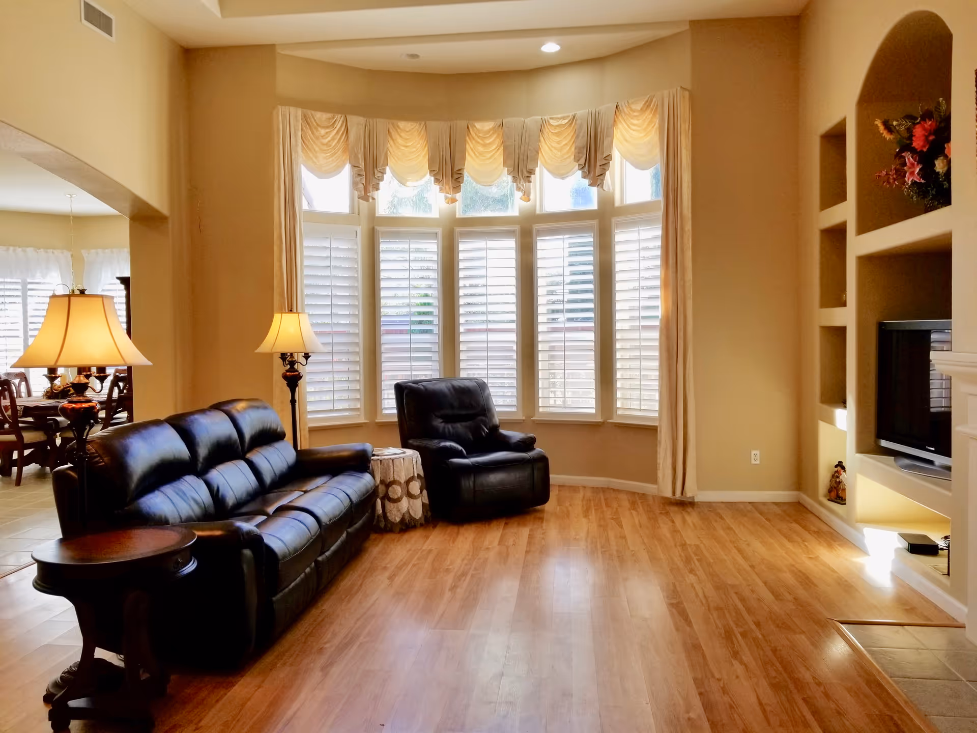 Bright living room with leather sofa, bay window, and built-in shelves surrounding a TV.
