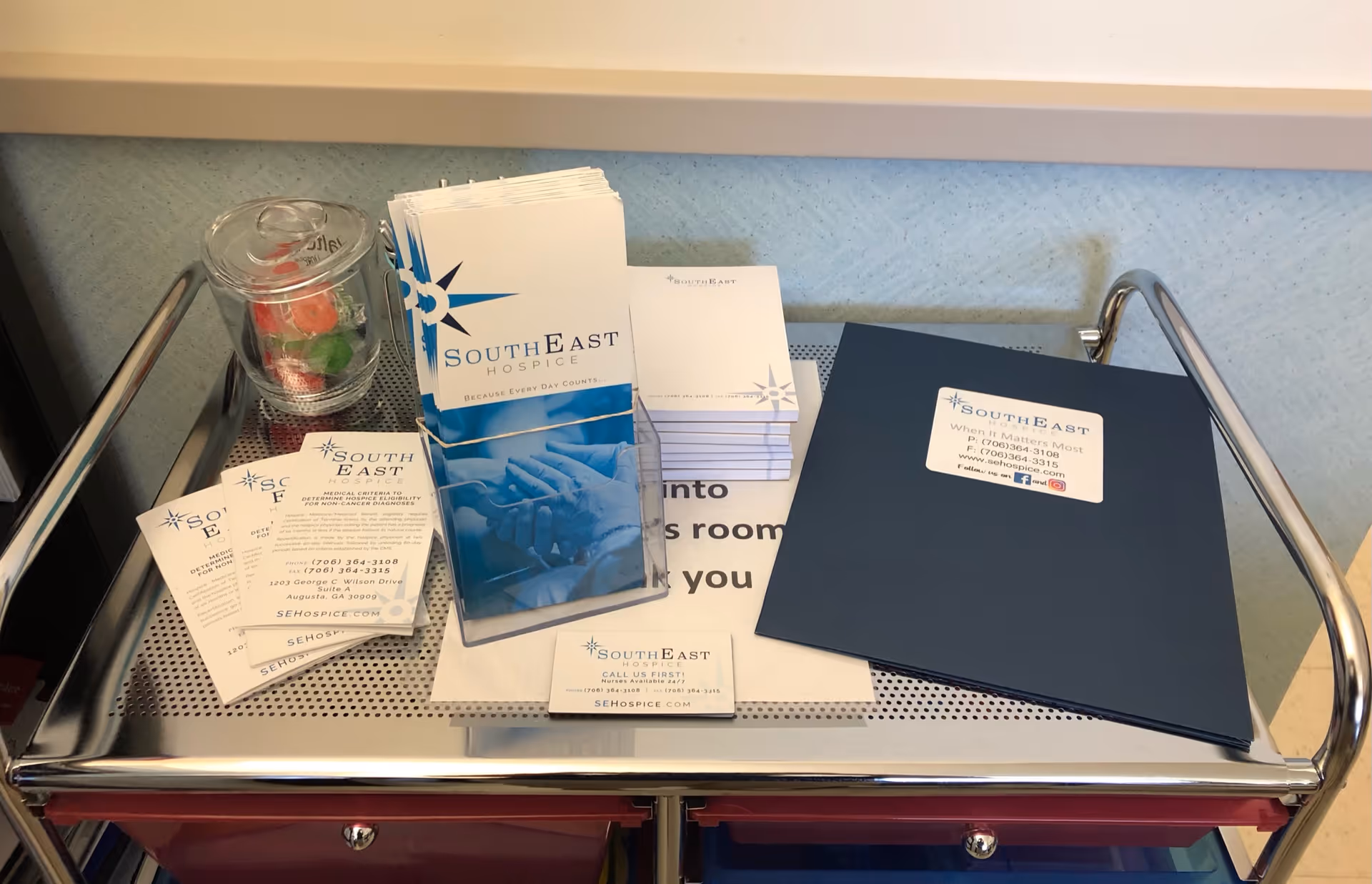 A metal cart holds Southeast Hospice brochures, business cards, and informational pamphlets in an interior.
