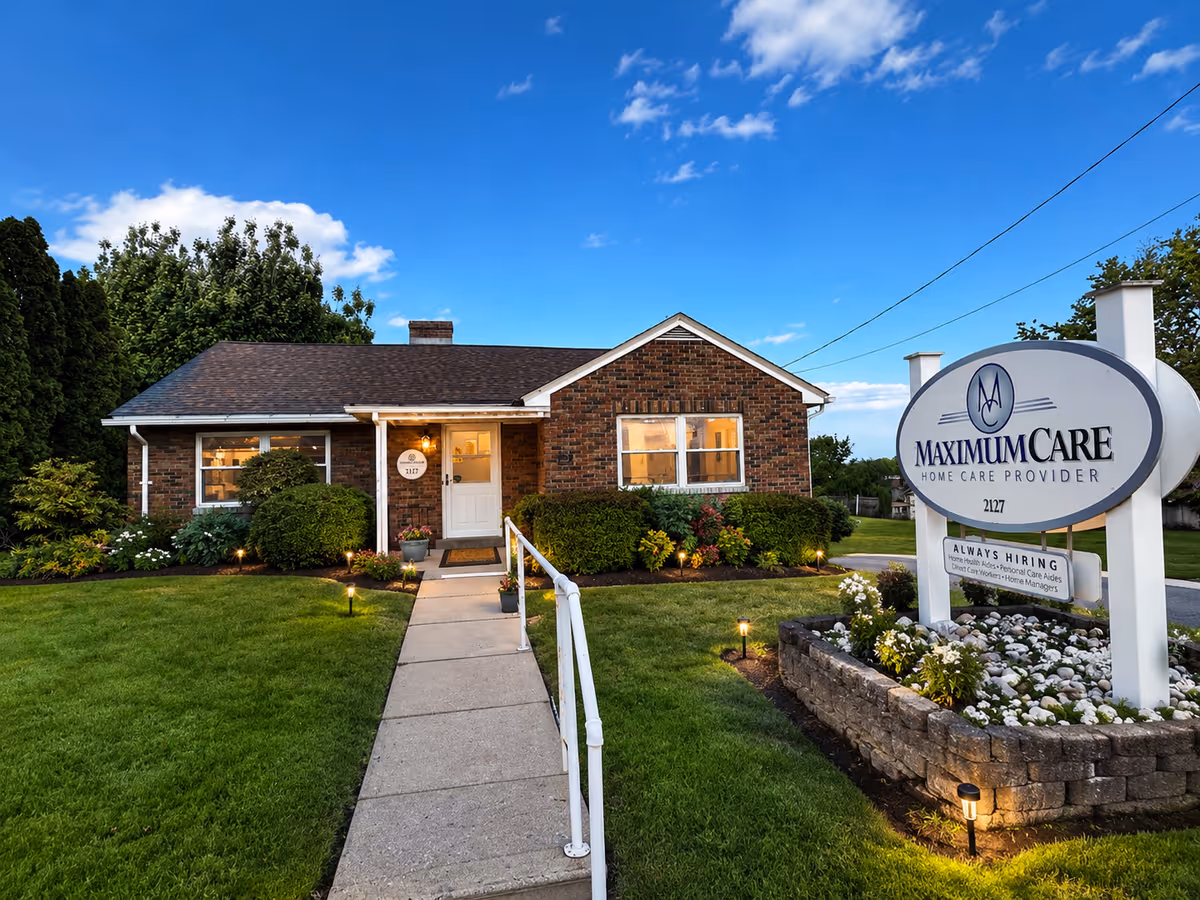 Brick, single-story facility with a neatly landscaped lawn, entrance walkway, and a large Maximum Care sign.