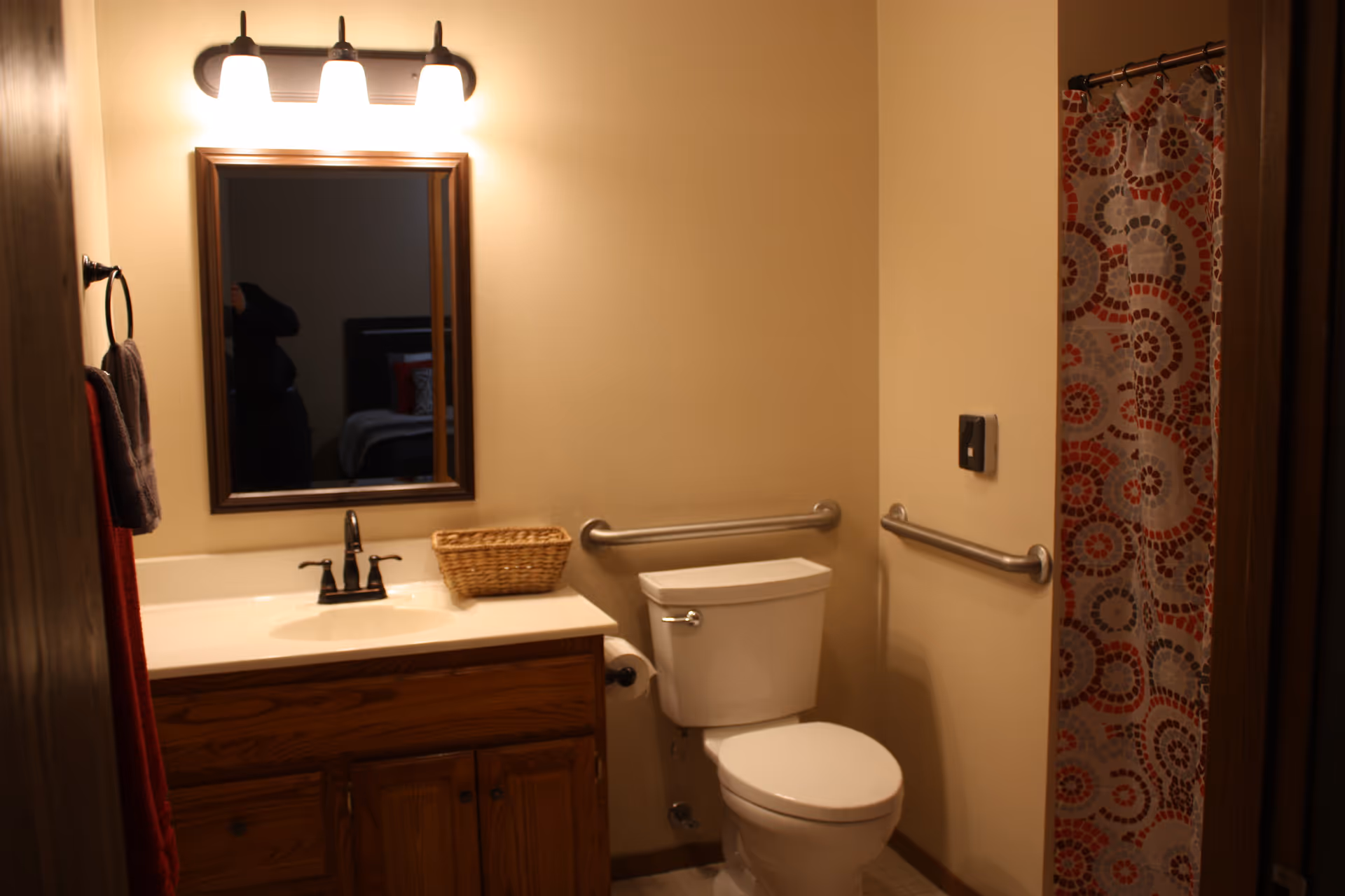 Bathroom with sink, mirror, toilet, grab bars, and patterned shower curtain.