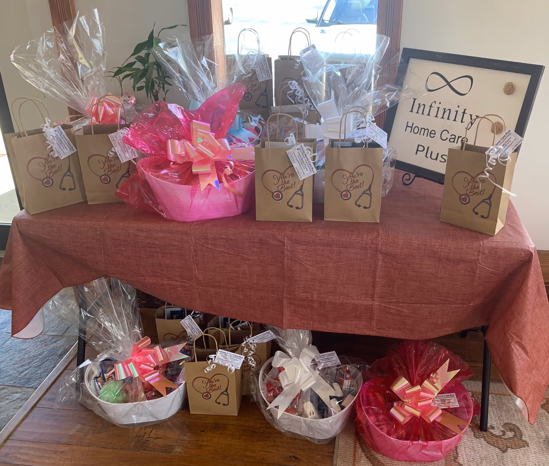Gift bags and baskets arranged on a table with Infinity Home Care Plus sign.
