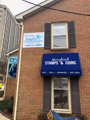 Brick building frontage with Visiting Angels sign and blue Maryland Stamps & Coins storefront.