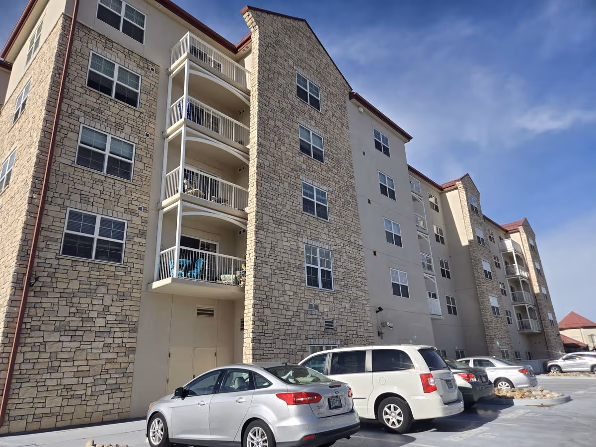 Exterior view of a multi-story stone-faced residential building with balconies and parked cars in front.