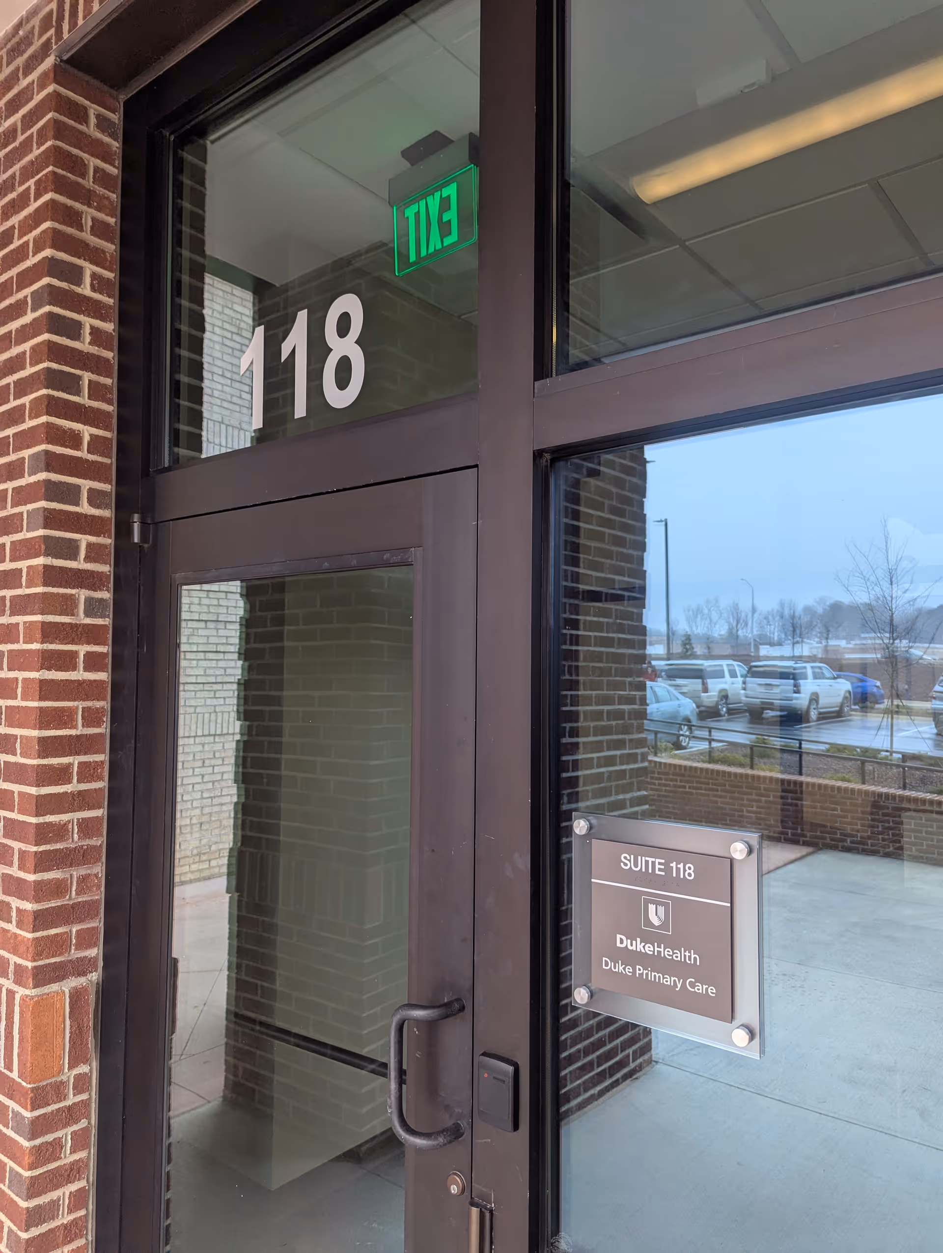 Front entrance of DukeHealth Suite 118 with brick facade and green exit sign
