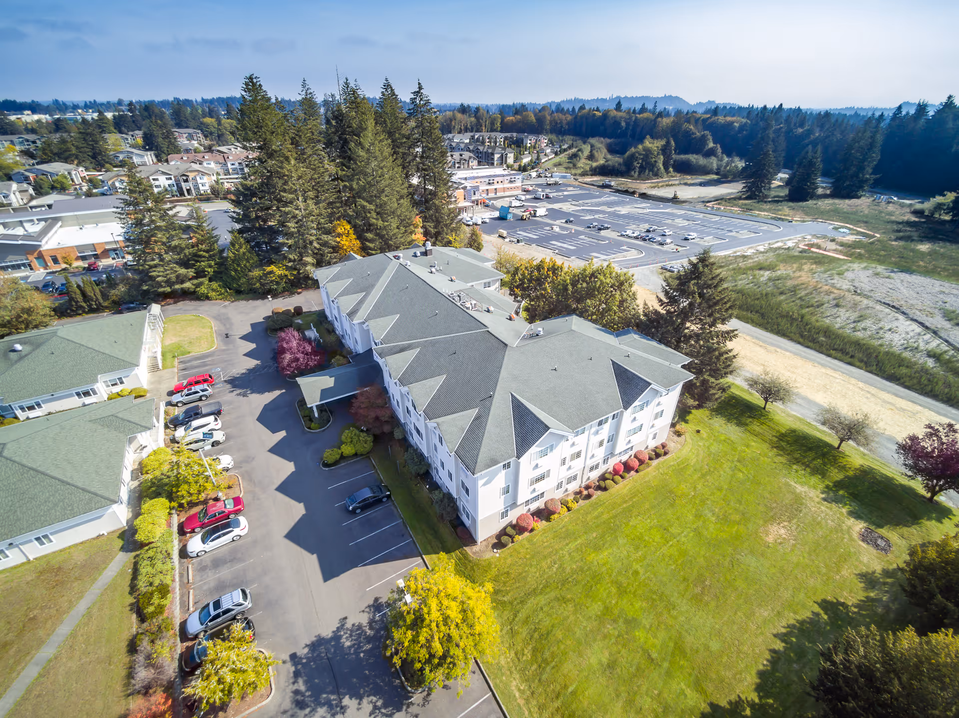 Aerial view of a multi-story assisted living building with parking, landscaped lawns and surrounding trees and development.