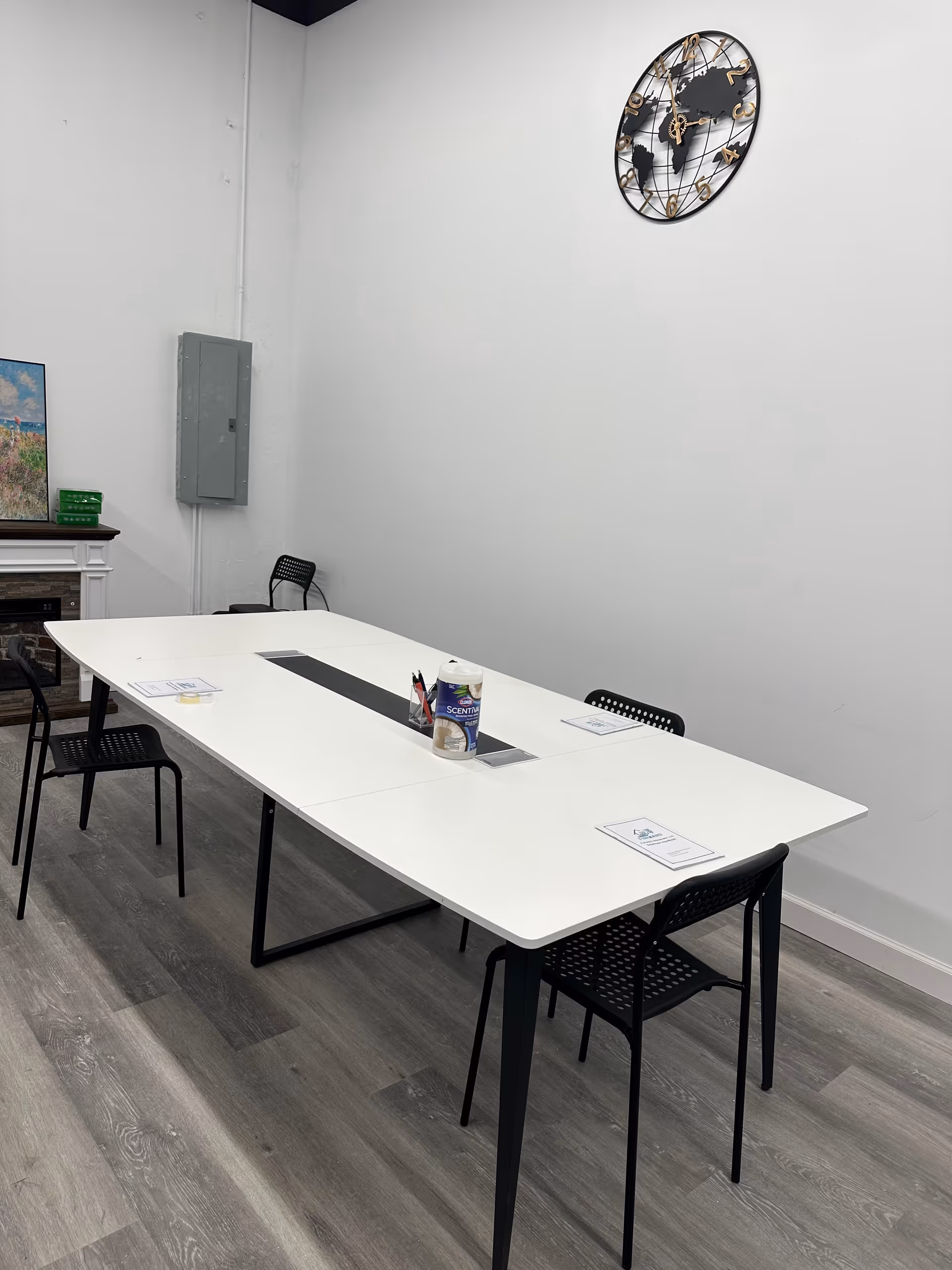 A minimalist conference room with a long white table, black chairs, and scattered papers.