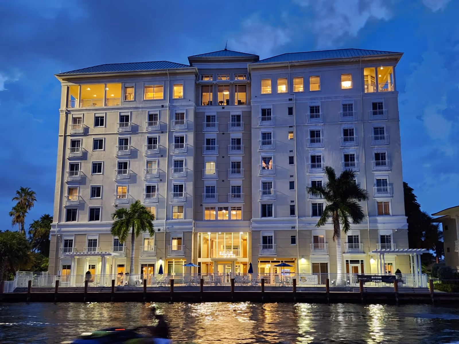 Exterior view of The Meridian at Waterways, a multi-story waterfront senior living building at dusk.