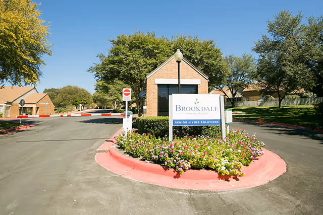 Entrance gatehouse and landscaped roundabout with a 'Brookdale' senior living sign at a community driveway.