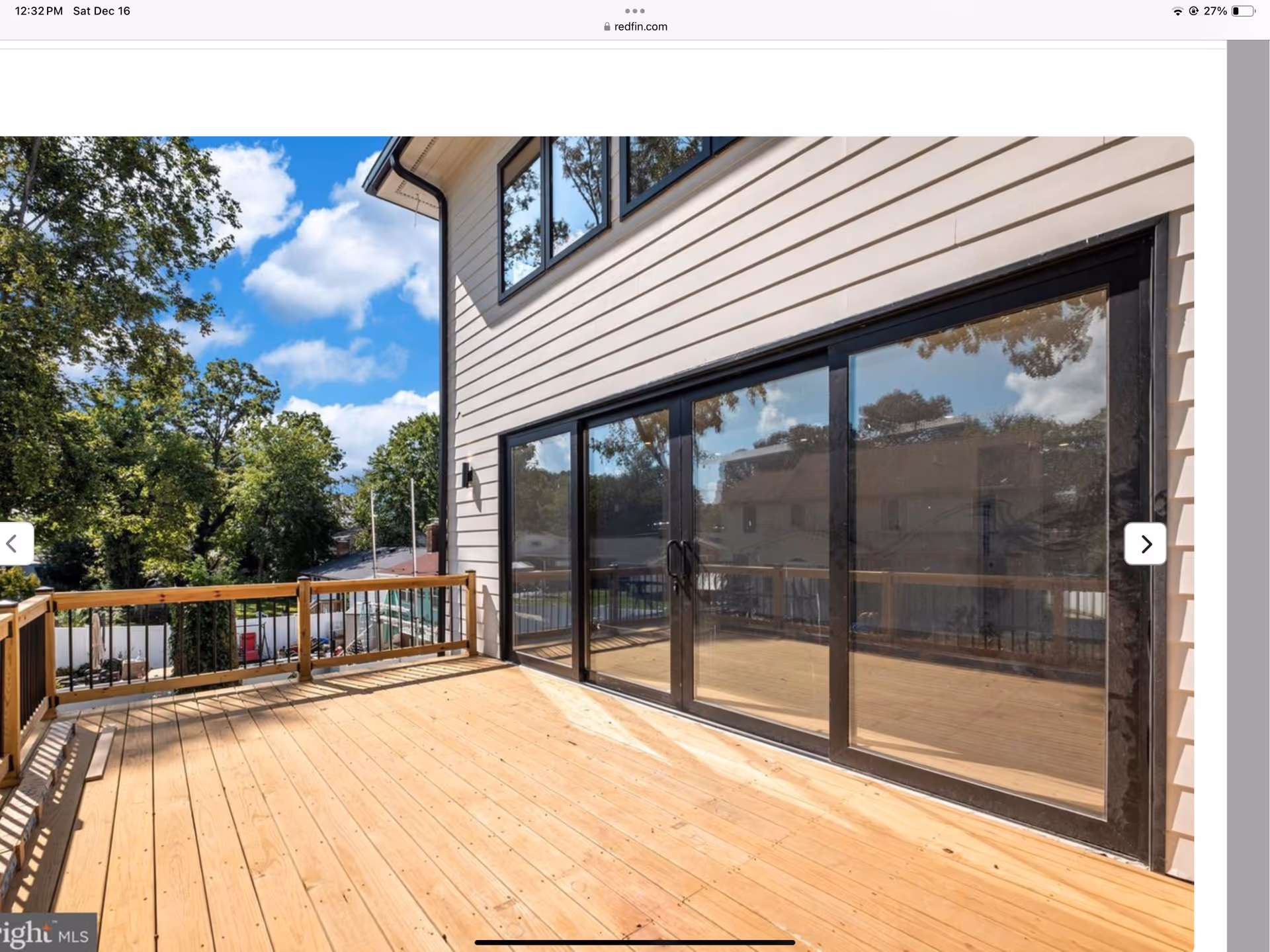 Outdoor wooden deck with large sliding glass doors, railing, and trees beyond.