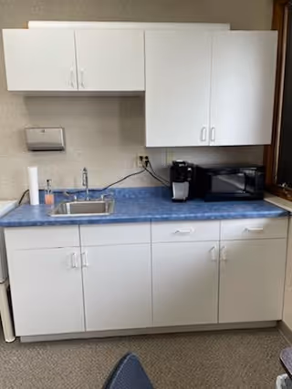 Small white kitchen with blue countertop, sink, paper towel roll, and coffee maker.