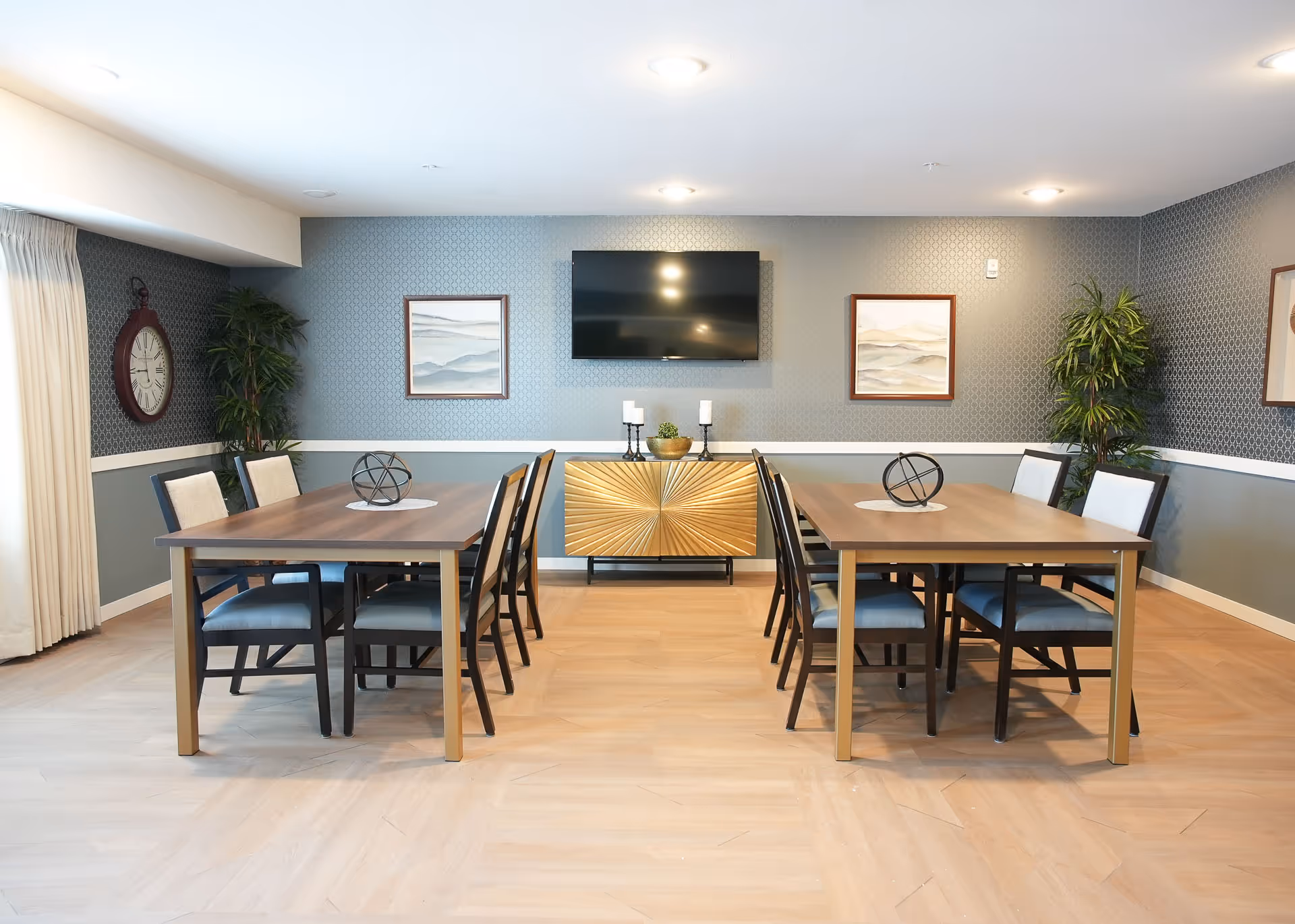 Two rectangular wooden dining tables surrounded by chairs in a bright, modern communal dining area.