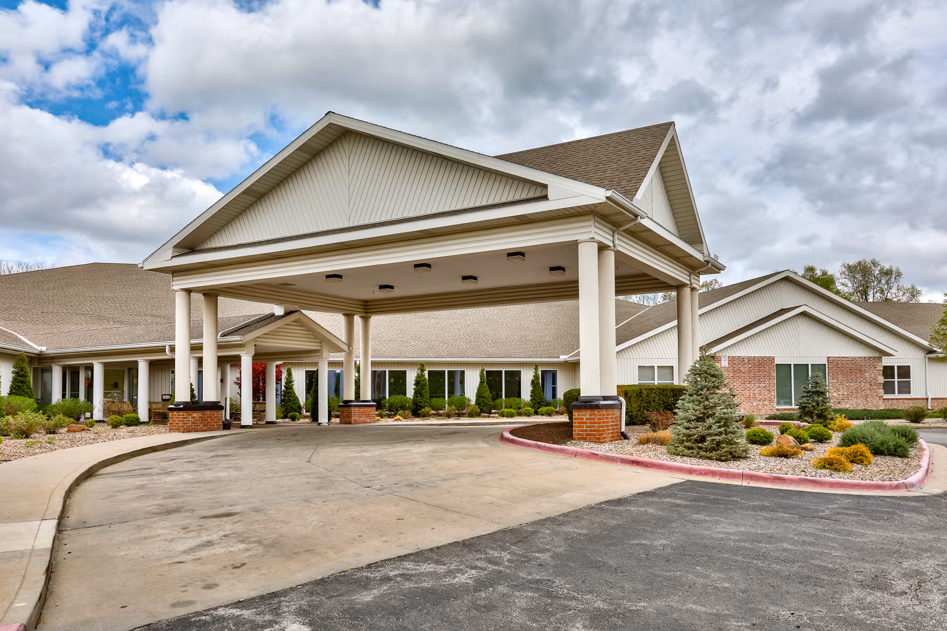 Exterior view of a senior living facility with a covered entry and landscaped front.
