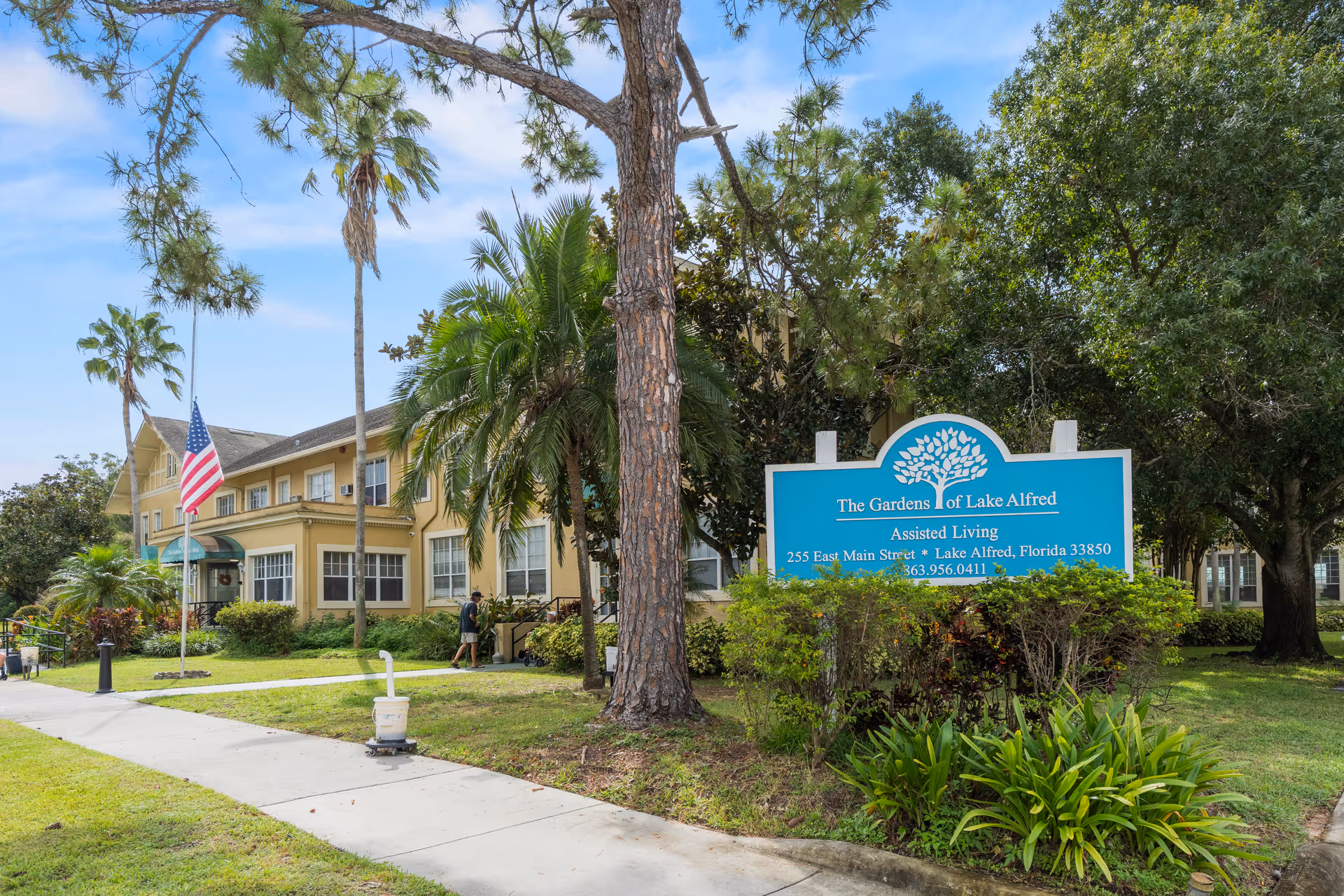 Exterior view of The Gardens of Lake Alfred with sign, building, and palm trees.