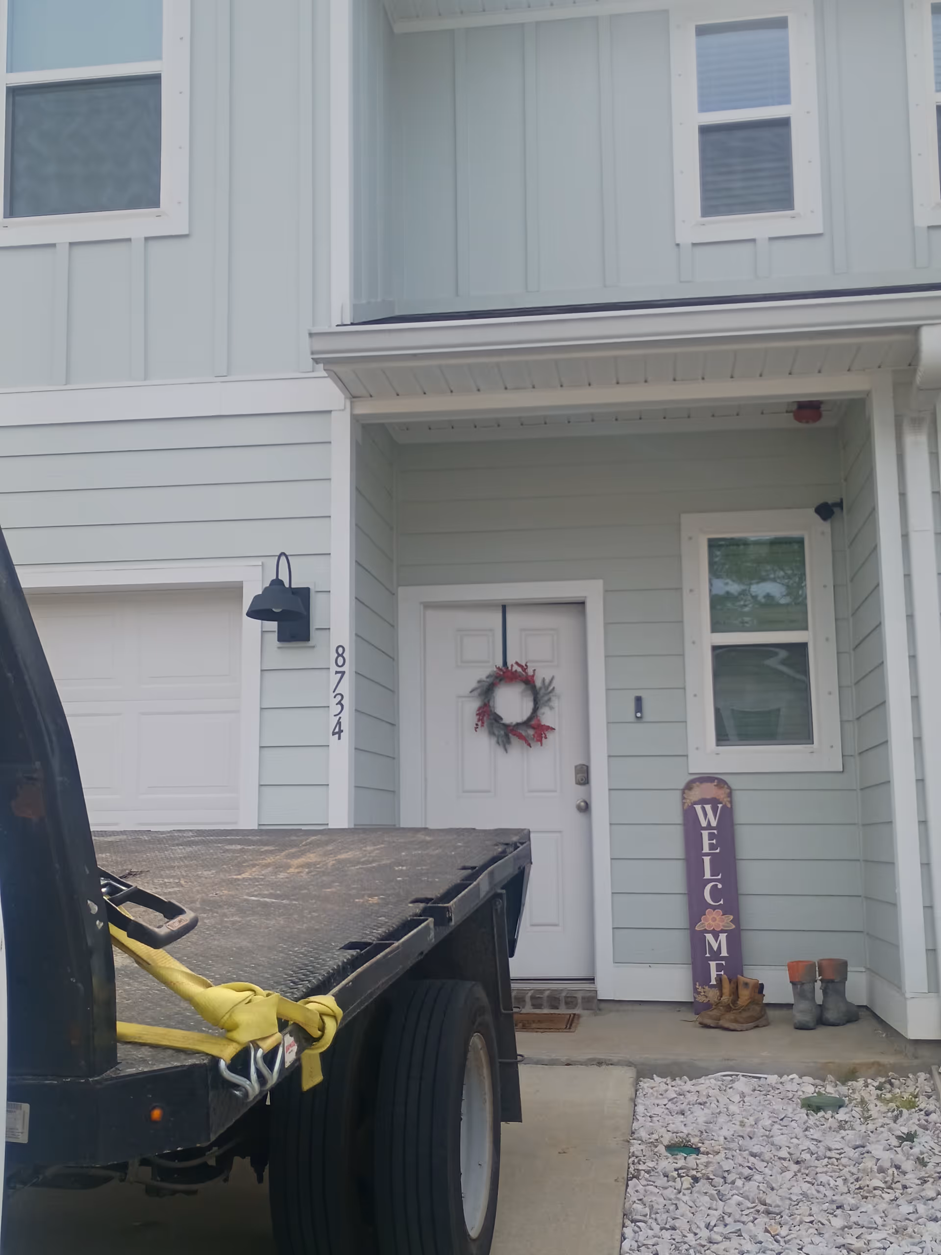 Front entrance of a light blue townhouse-style building with a wreath and welcome sign.