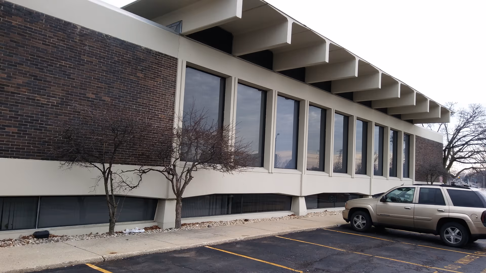 Exterior of a long building with large windows and a parked SUV nearby.
