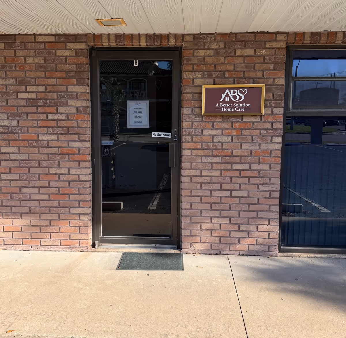Brick exterior entrance with glass door and ABS A Better Solution Home Care sign.
