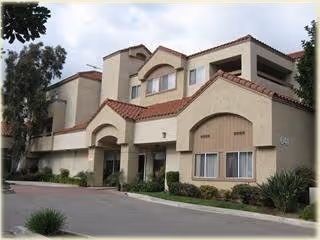 Exterior view of a beige, multi-story senior living building with a red-tiled roof.