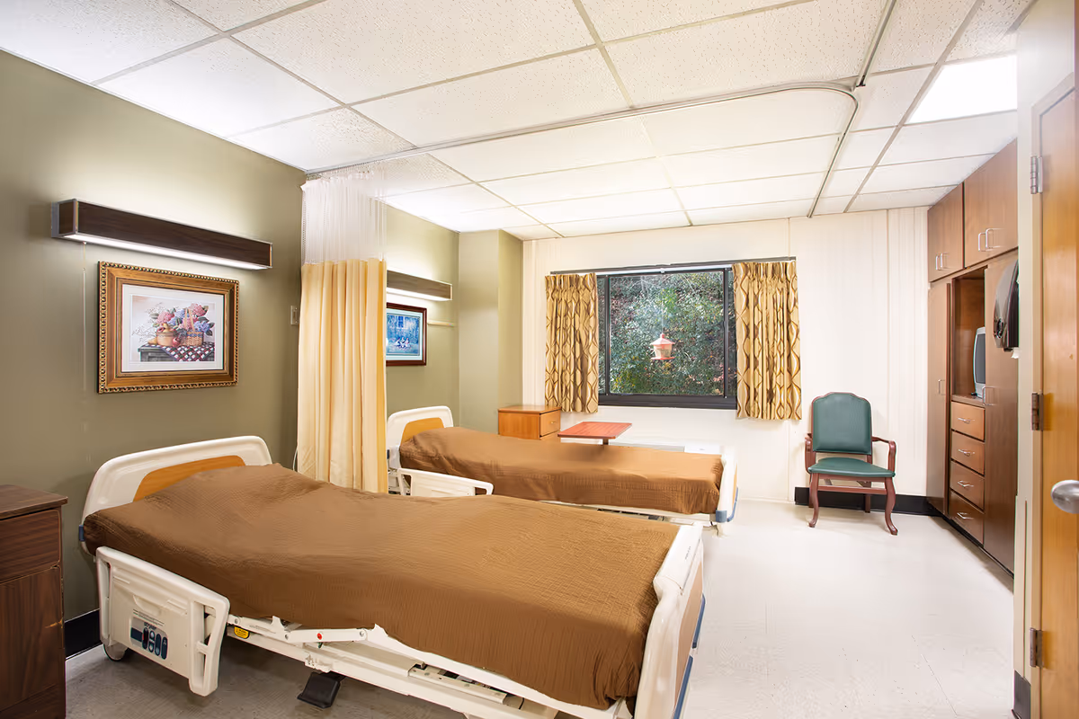 Two hospital-style beds in a shared patient room with window and curtains.