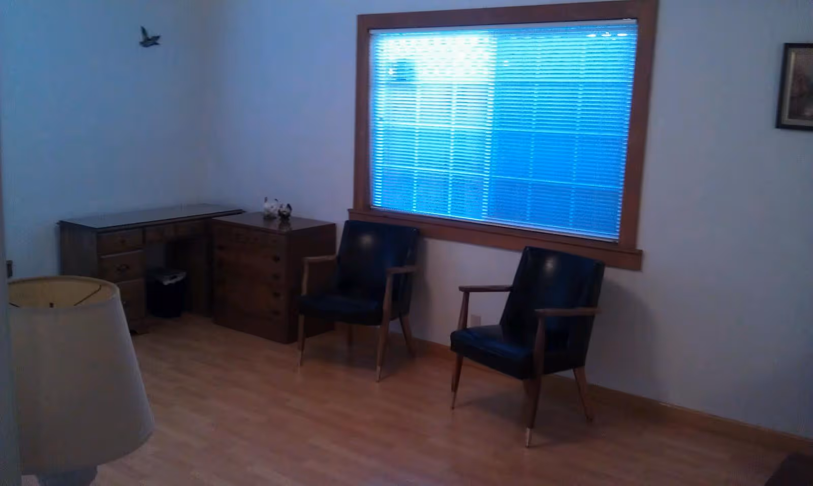 A simple senior living lounge with two black chairs, a desk, and a large window.