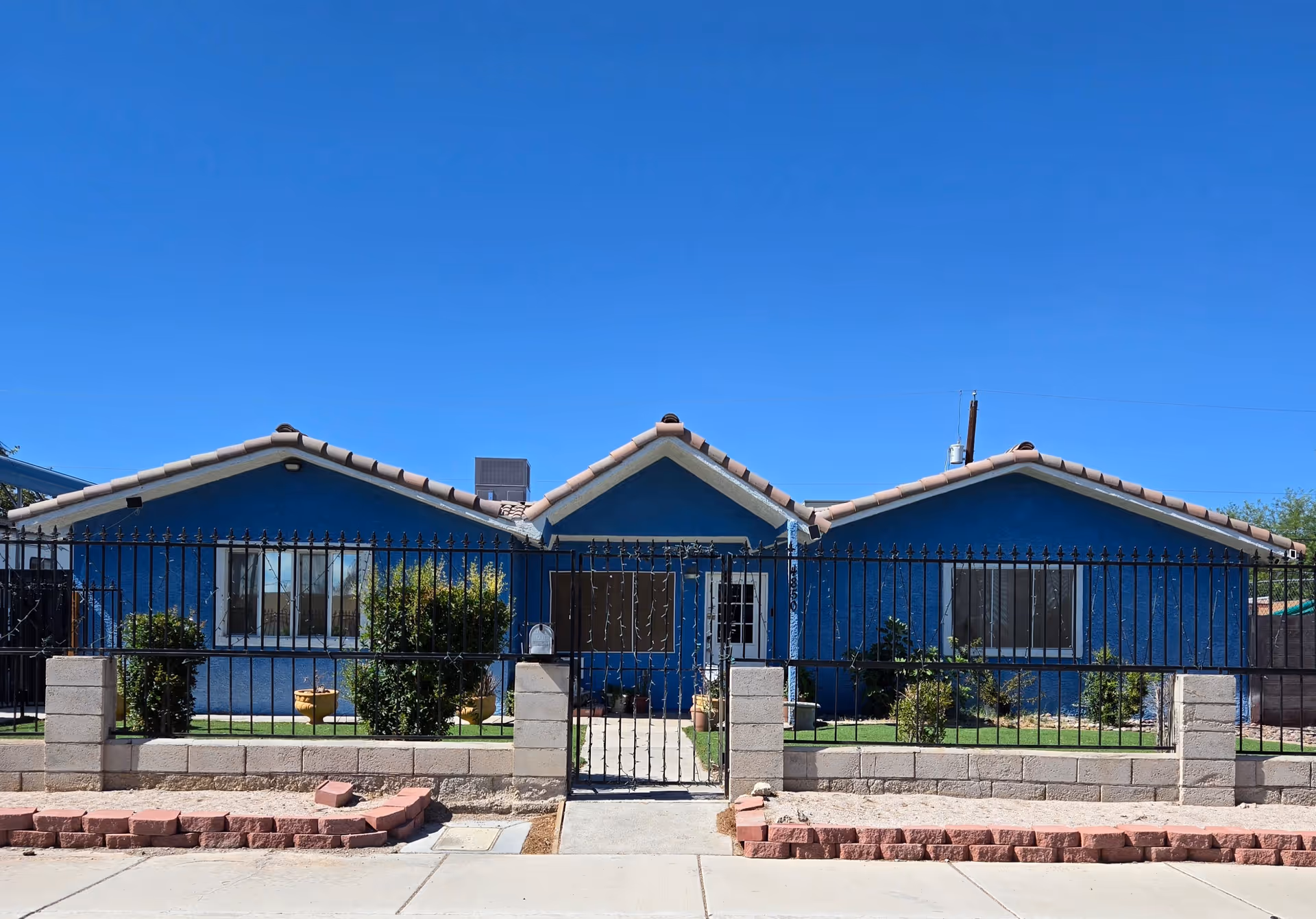 A bright blue single-story building with a black wrought-iron fence and a gated front yard.